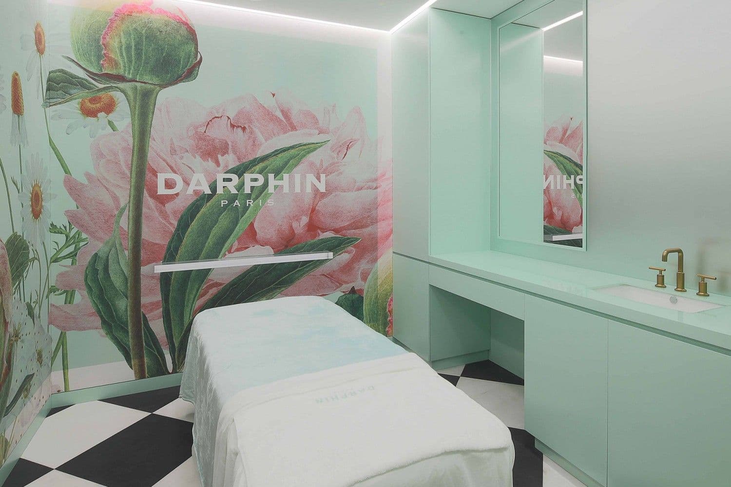 Treatment room with a pastel floral mural of tulips behind a spa bed, mint-green cabinetry, and mirrored wall.