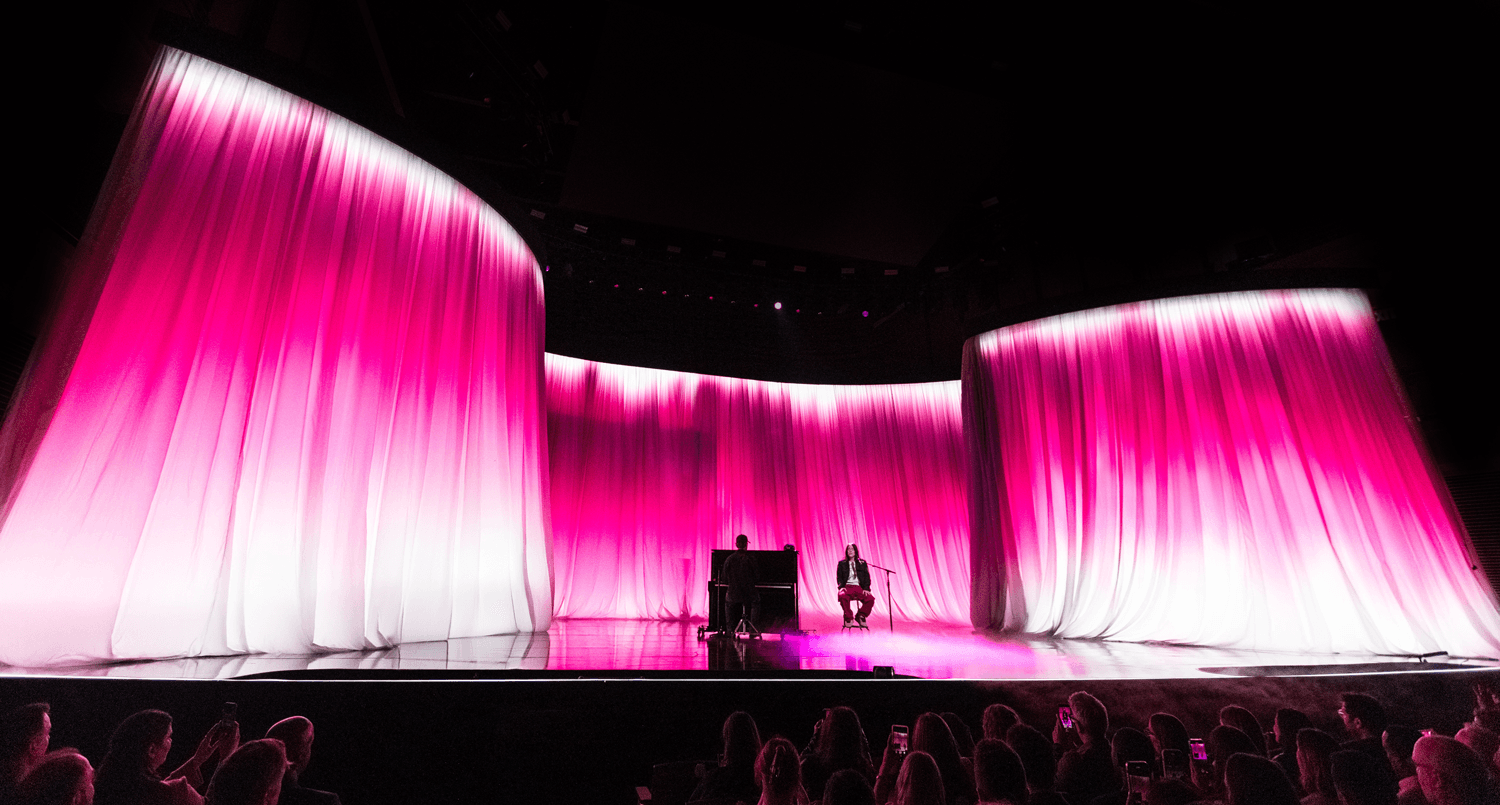 Wide view of pink-lit draped curtain panels framing an empty stage
