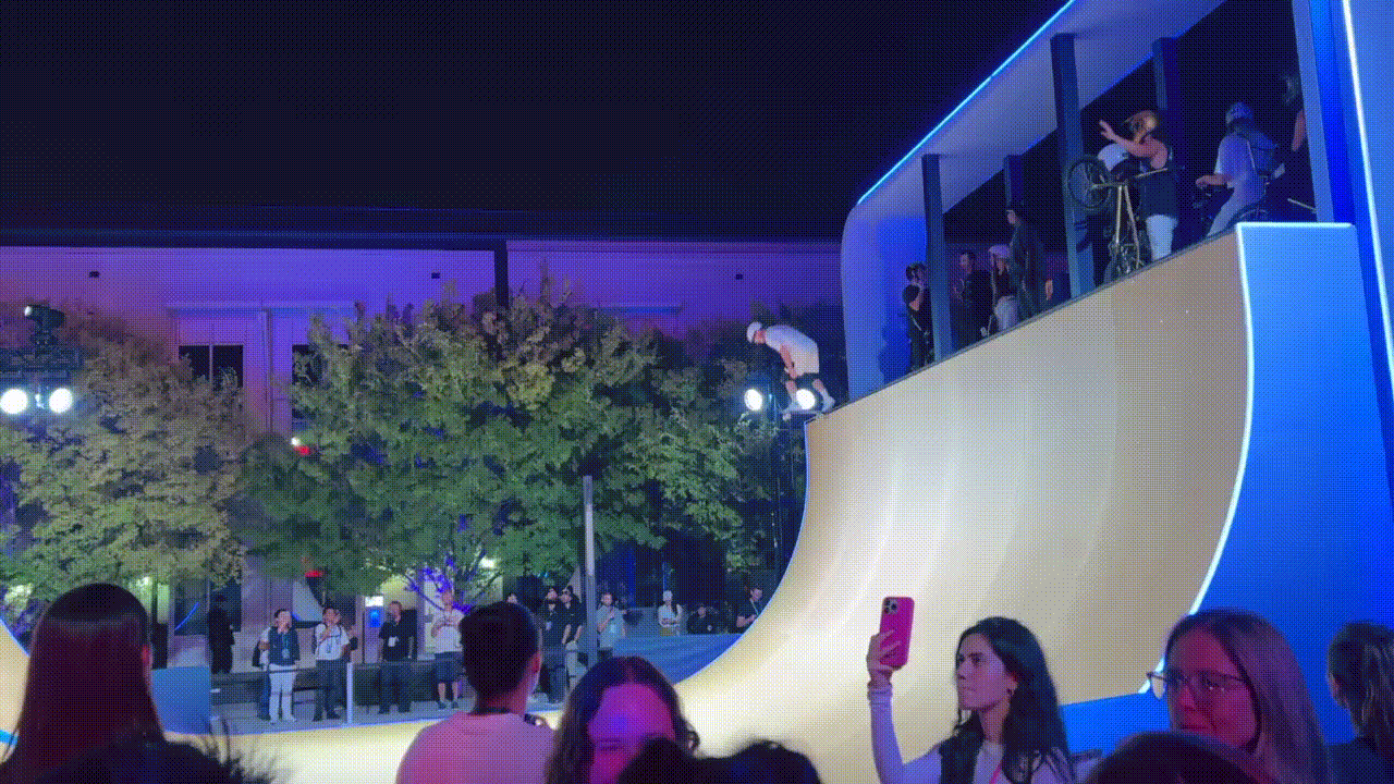 Skateboarder mid-air above a halfpipe ramp at night in front of a crowd.