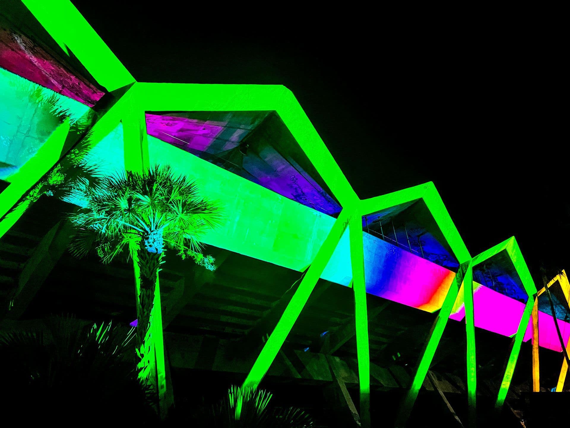 Rainbow light beams from the installation reflecting across the water with a city skyline in the background