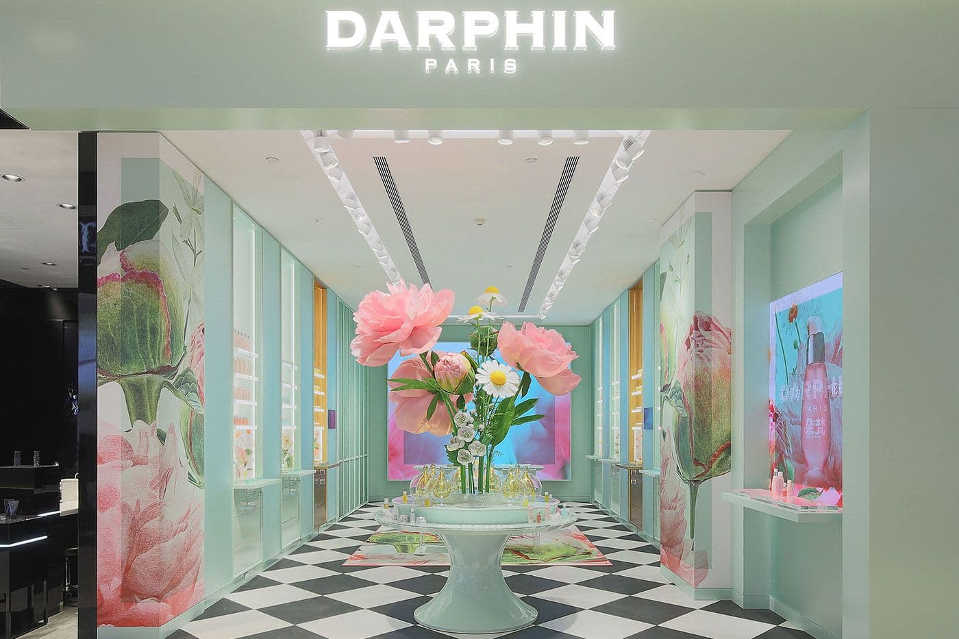 Darphin Paris storefront corridor with a large peony floral mural, mint-green display cases, and black-and-white checkerboard flooring.