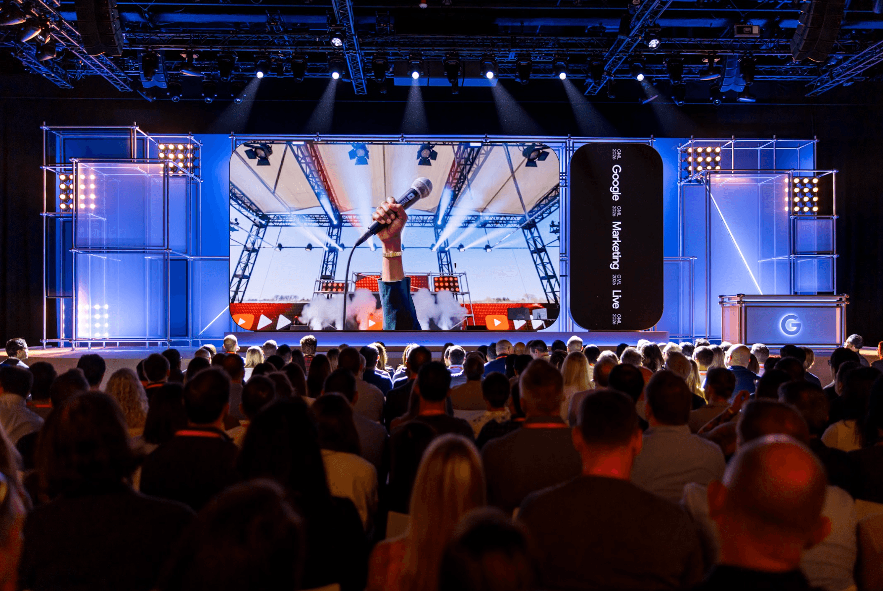Dark conference stage with dramatic blue lighting, a speaker presenting to a seated audience.