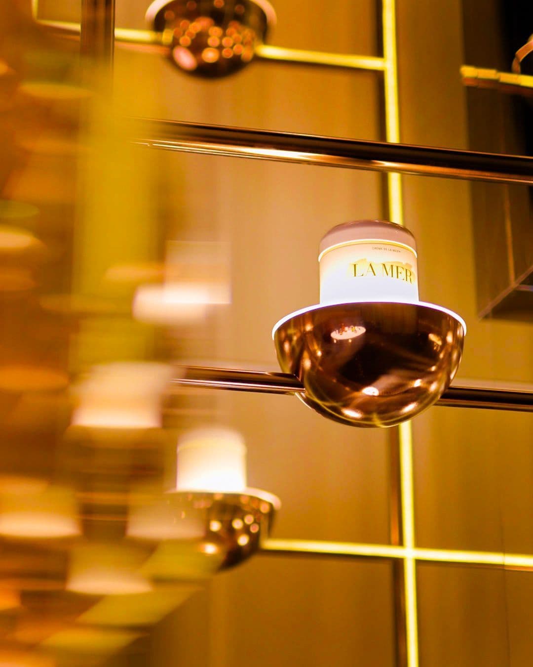 Close-up of a La Mer jar suspended among a grid of brass display rods.
