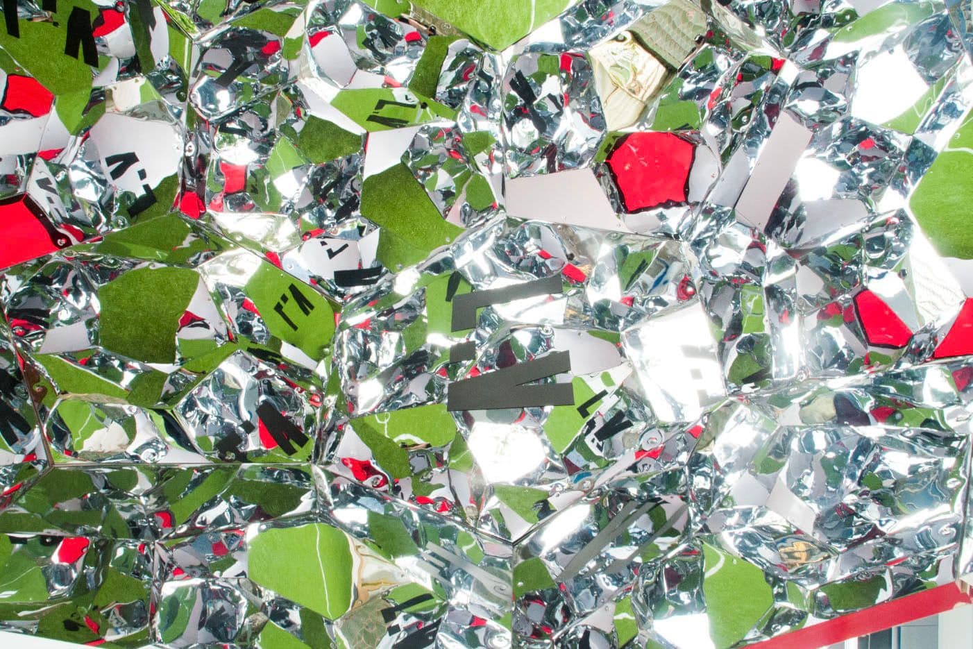Close-up of a shattered mirrored mosaic surface with green and red fragments.