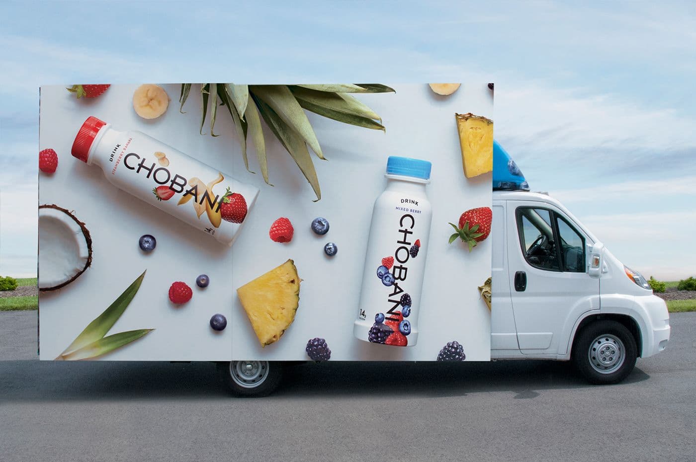 Overhead flat-lay of Chobani yogurt drink bottles and fresh fruit next to the parked truck.