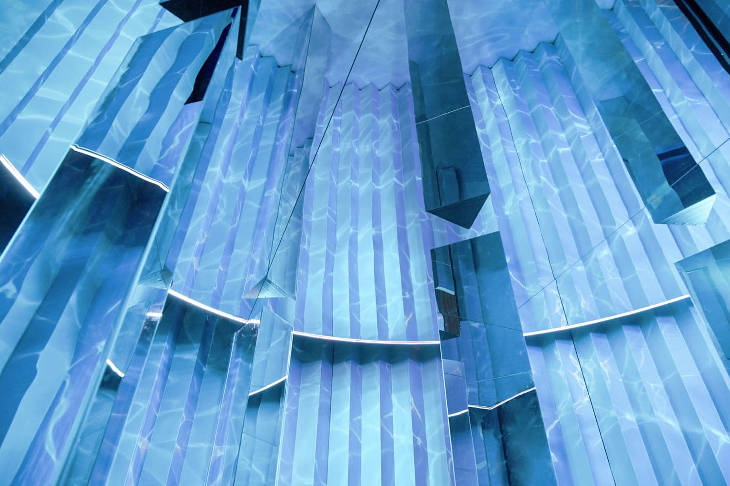 Blue-lit installation of angular mirrored panels resembling folded metallic sails.