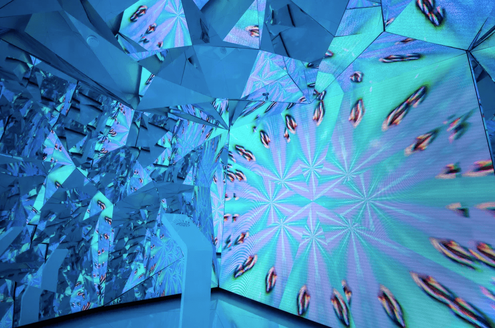 An empty kaleidoscopic mirrored tunnel lit in teal and blue tones.