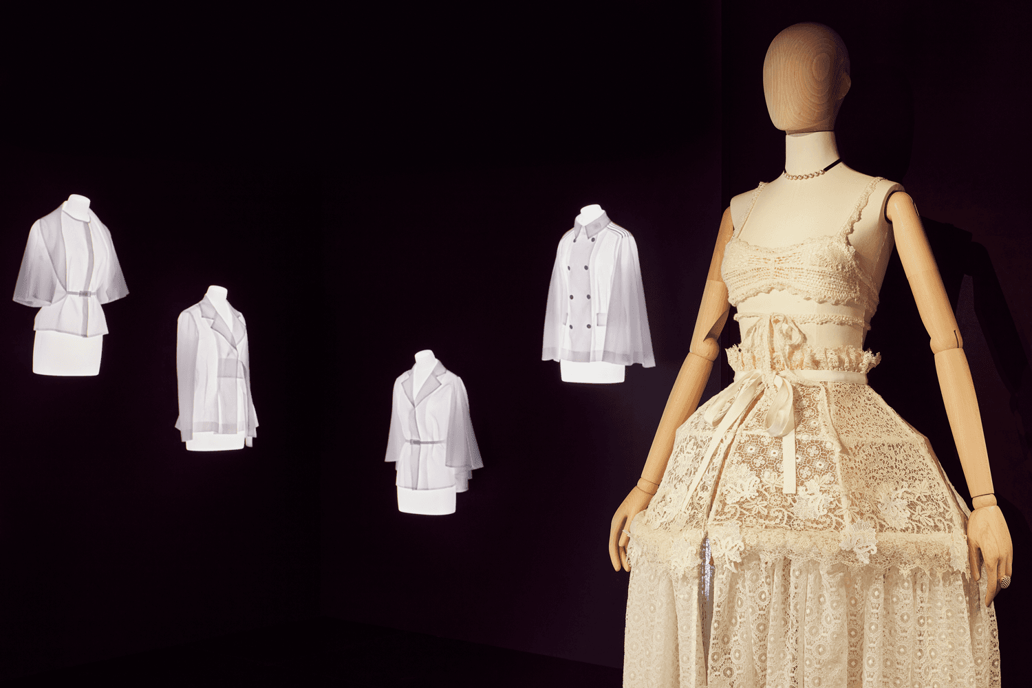 White dresses and shirts displayed on mannequins against a dark background.