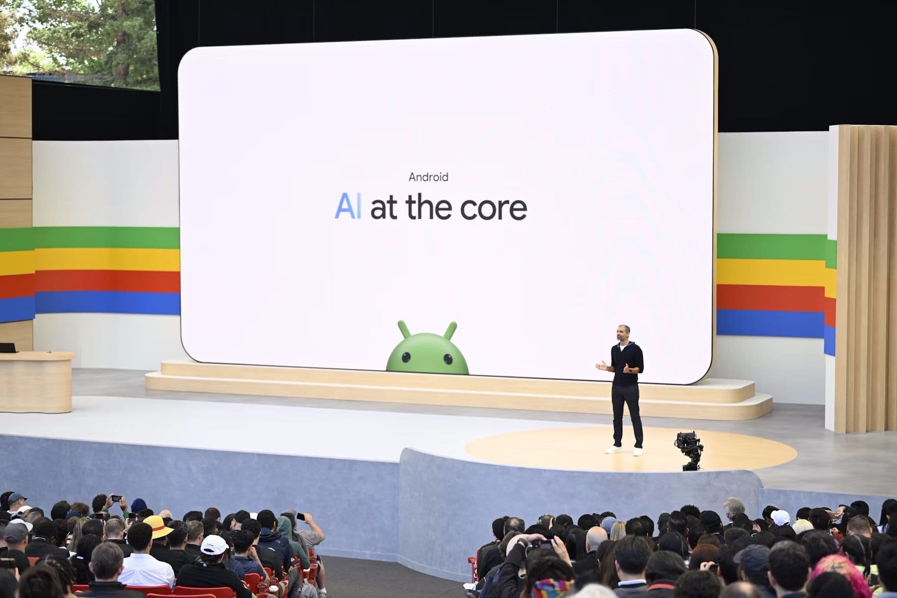 Presenter beside a screen reading 'AI at the core' with the Android logo, audience seated below.