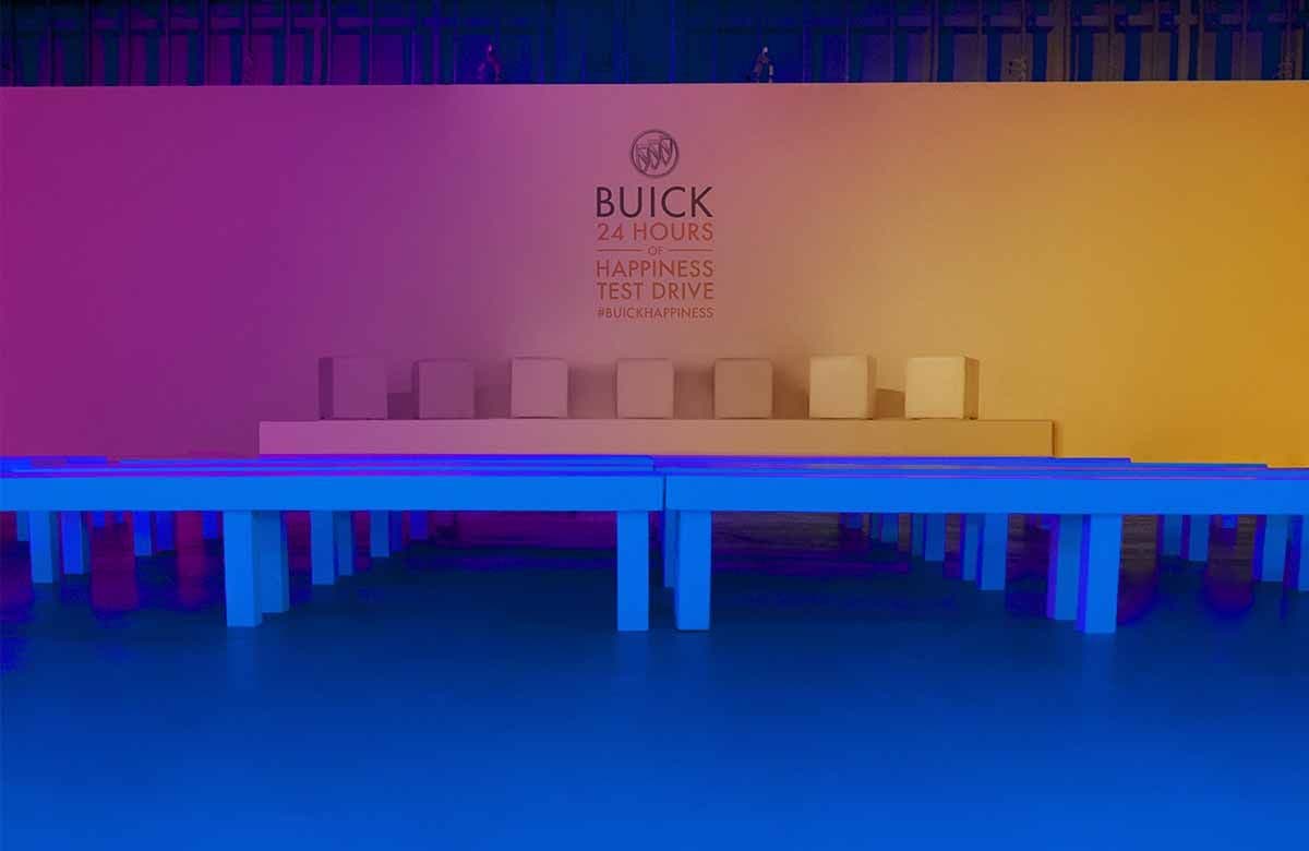 Buick "24 Hours of Happiness" test drive signage on a gradient wall above rows of blue-lit bench seating.