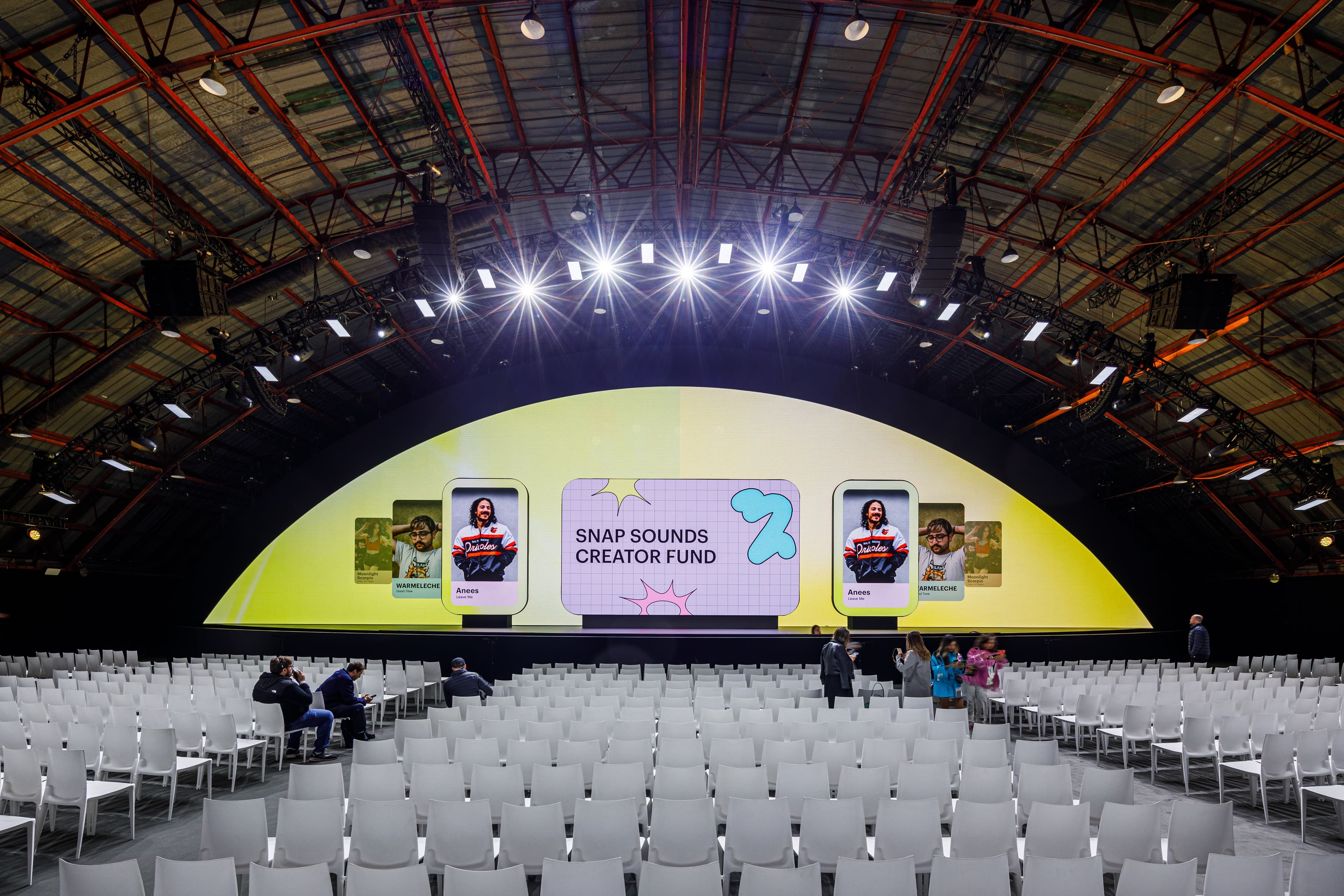 Arched event tent interior set up for a keynote, rows of empty chairs facing a stage screen.