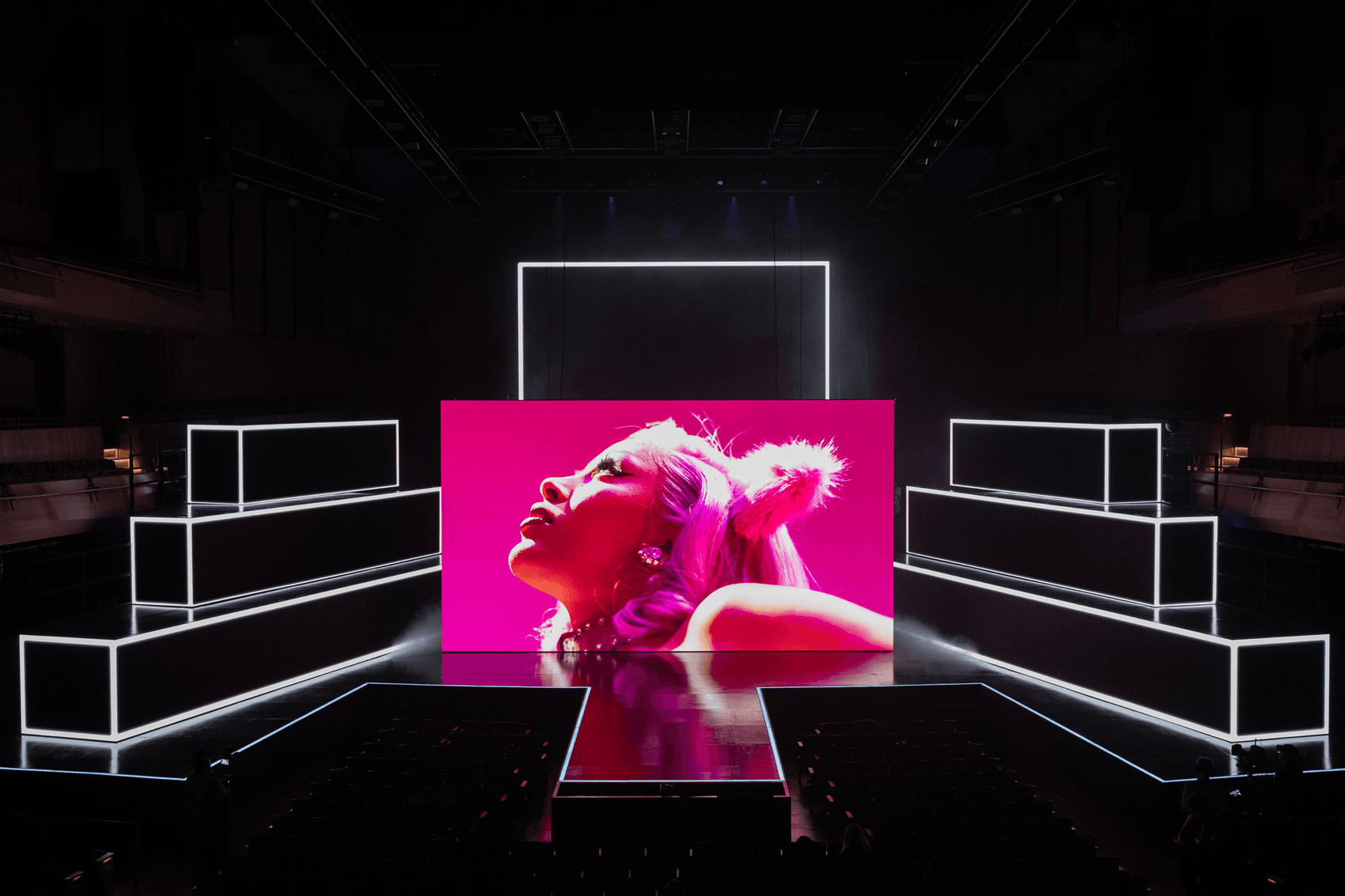 Performer in a pink spotlight on a white geometric stage set