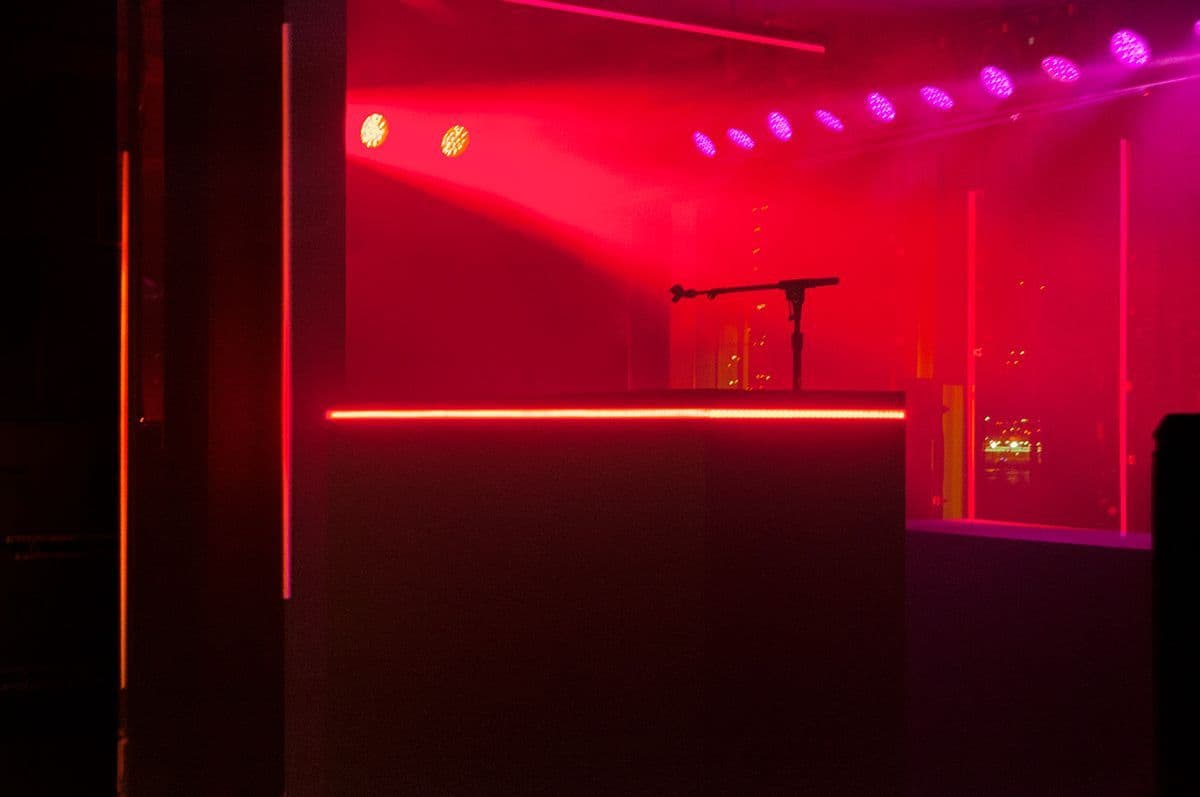 Red-lit stage area with a raised platform, overhead spotlights, and a microphone stand.