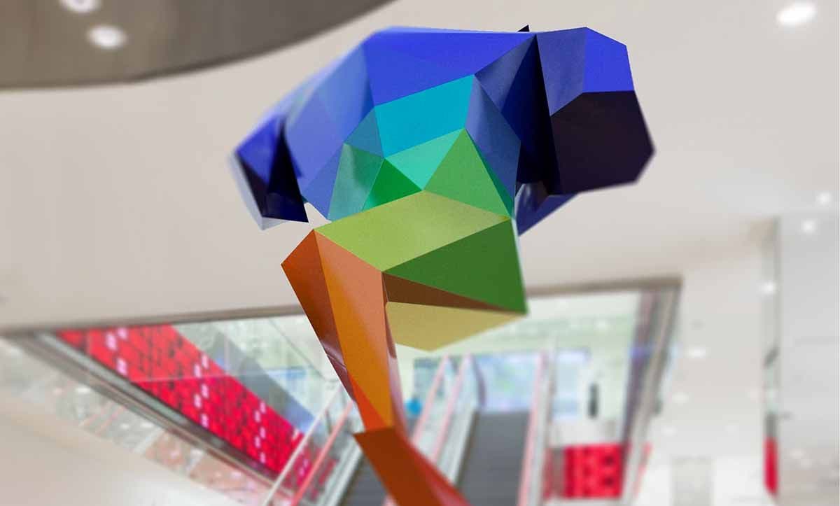 Multicolored faceted low-poly sculpture with an orange tail suspended in a mall atrium above red-paneled escalators.