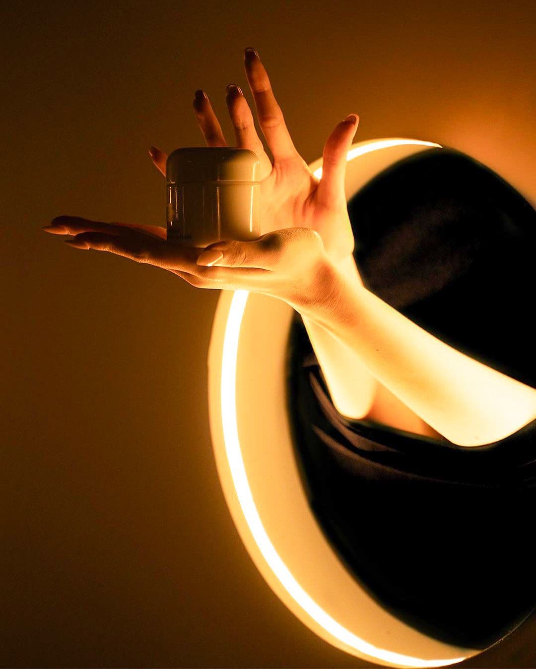 Close-up of a hand reaching through a circular cutout lit with warm orange light.