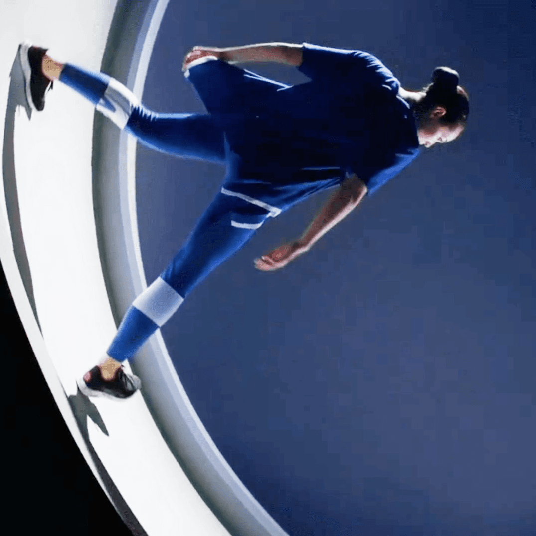 Person in a blue running outfit sprinting along the curved wall of an illuminated white ring set.