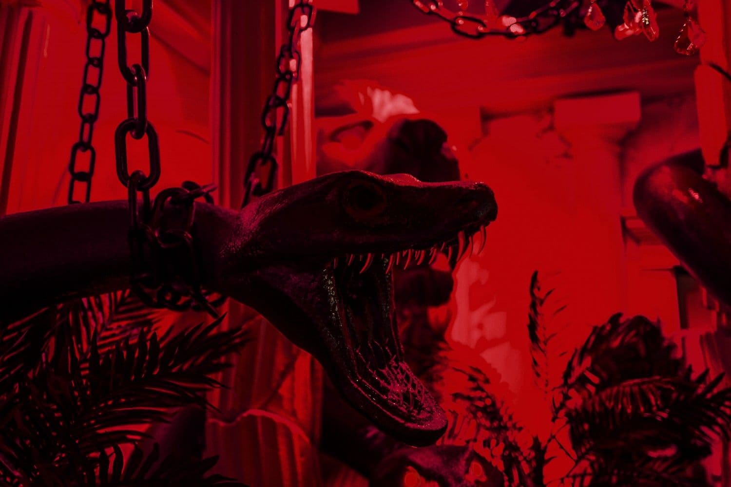 A red-lit room with a chained dinosaur skull sculpture beneath a classical archway.