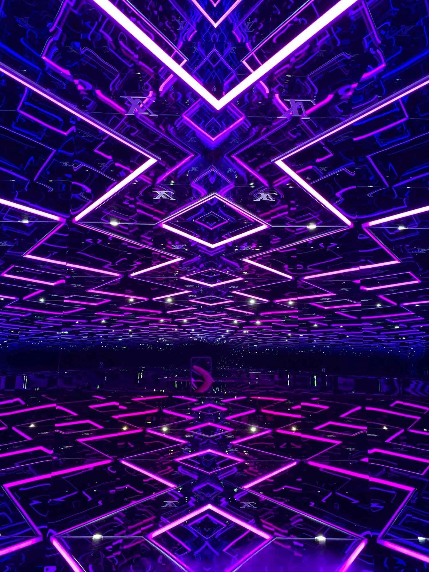Dark tunnel with a symmetrical purple and violet diamond-patterned light installation.