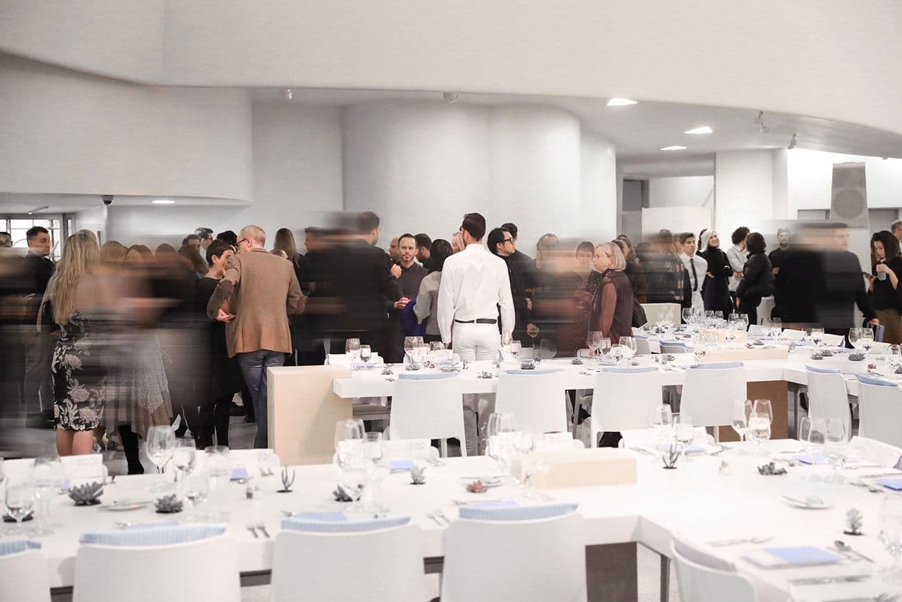 Blurred crowd of people mingling among white dinner tables set up in the museum's rotunda lobby