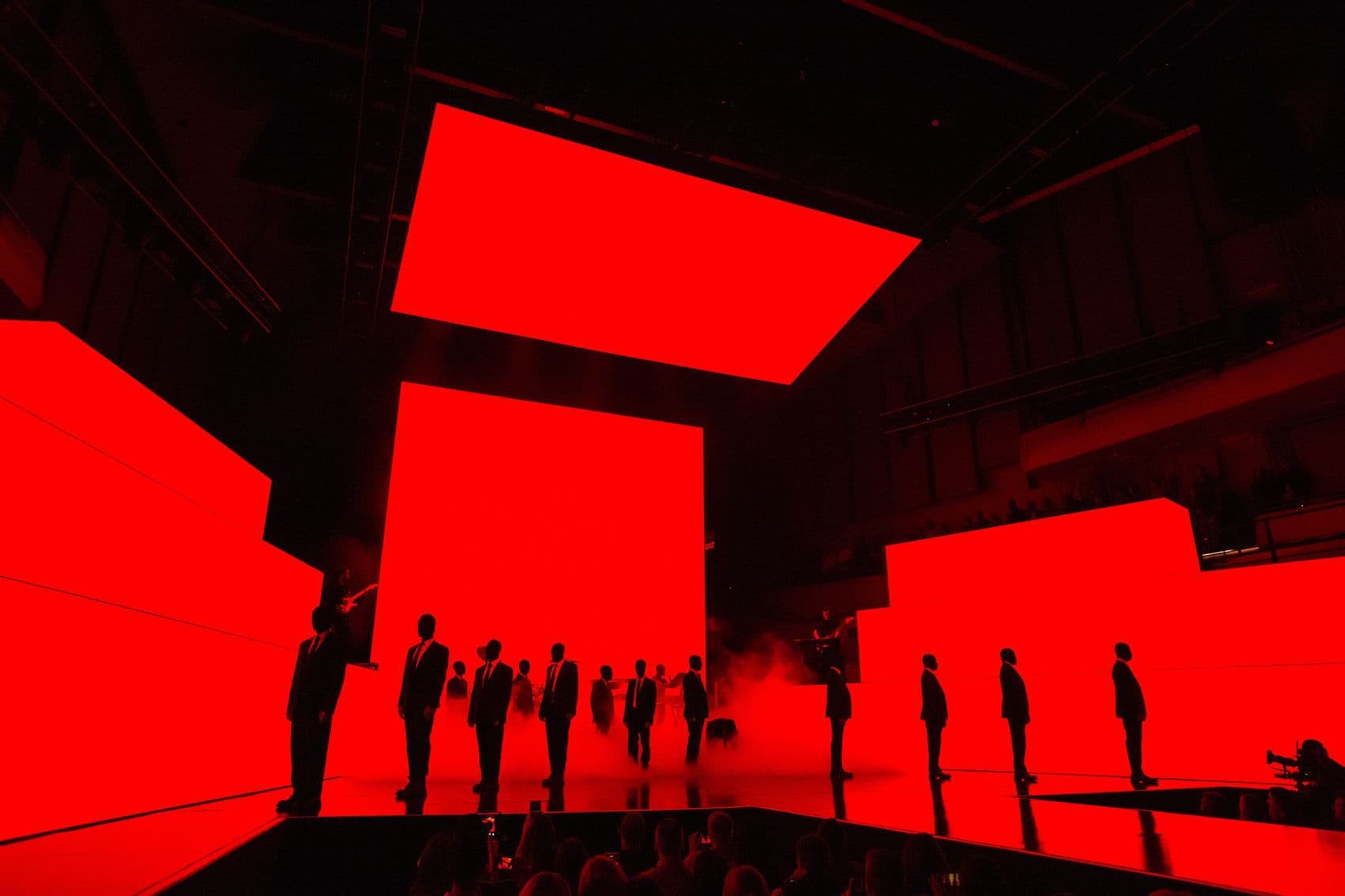 Silhouetted figures standing in a row against a red-lit stage backdrop