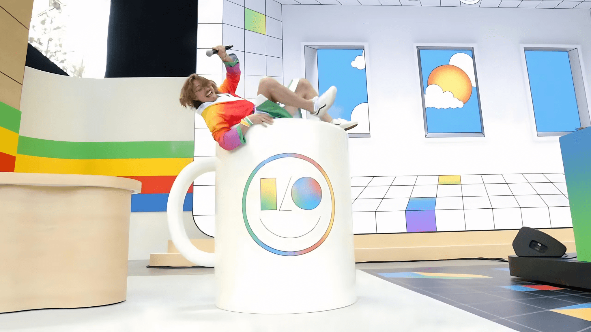 Oversized Google-branded mug filled with plush toy characters on a stage set with colorful window graphics.