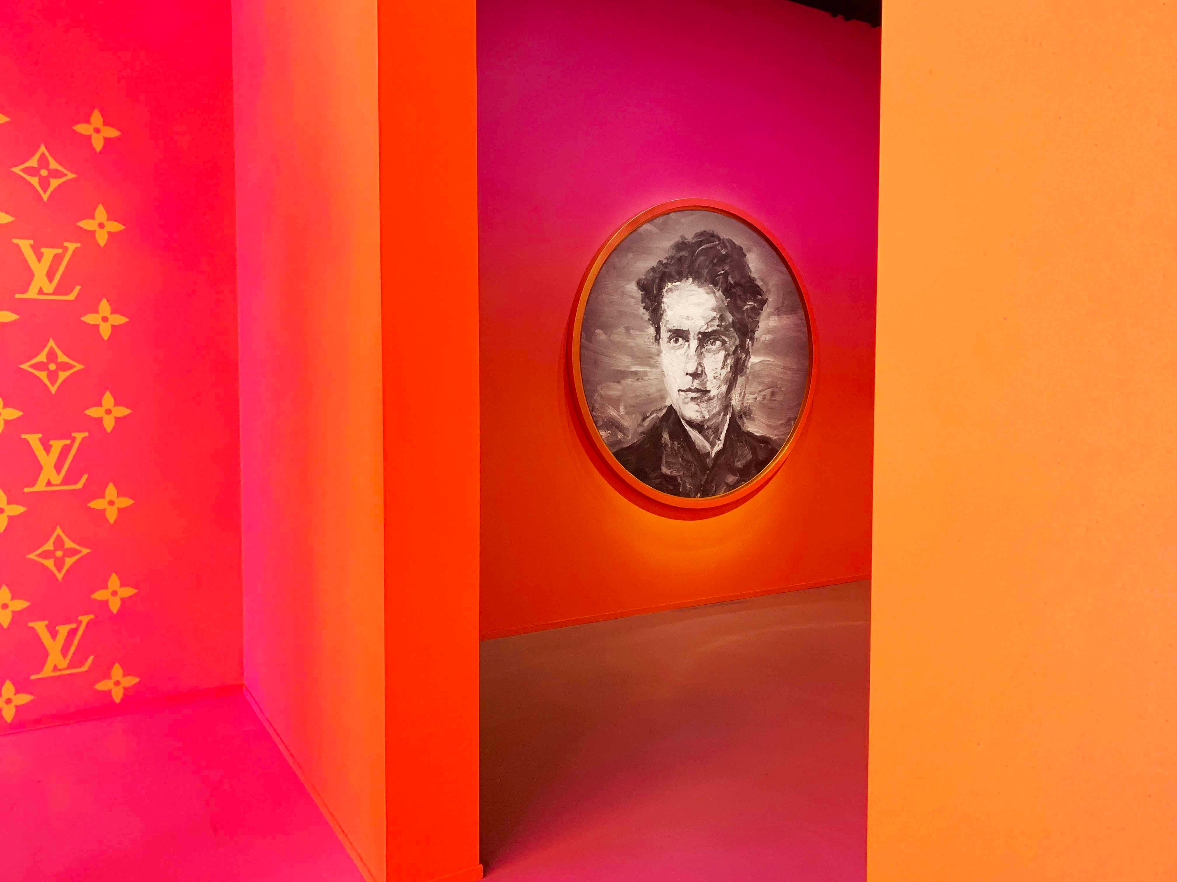 Pink archway framing a round sepia portrait painting against an orange wall.