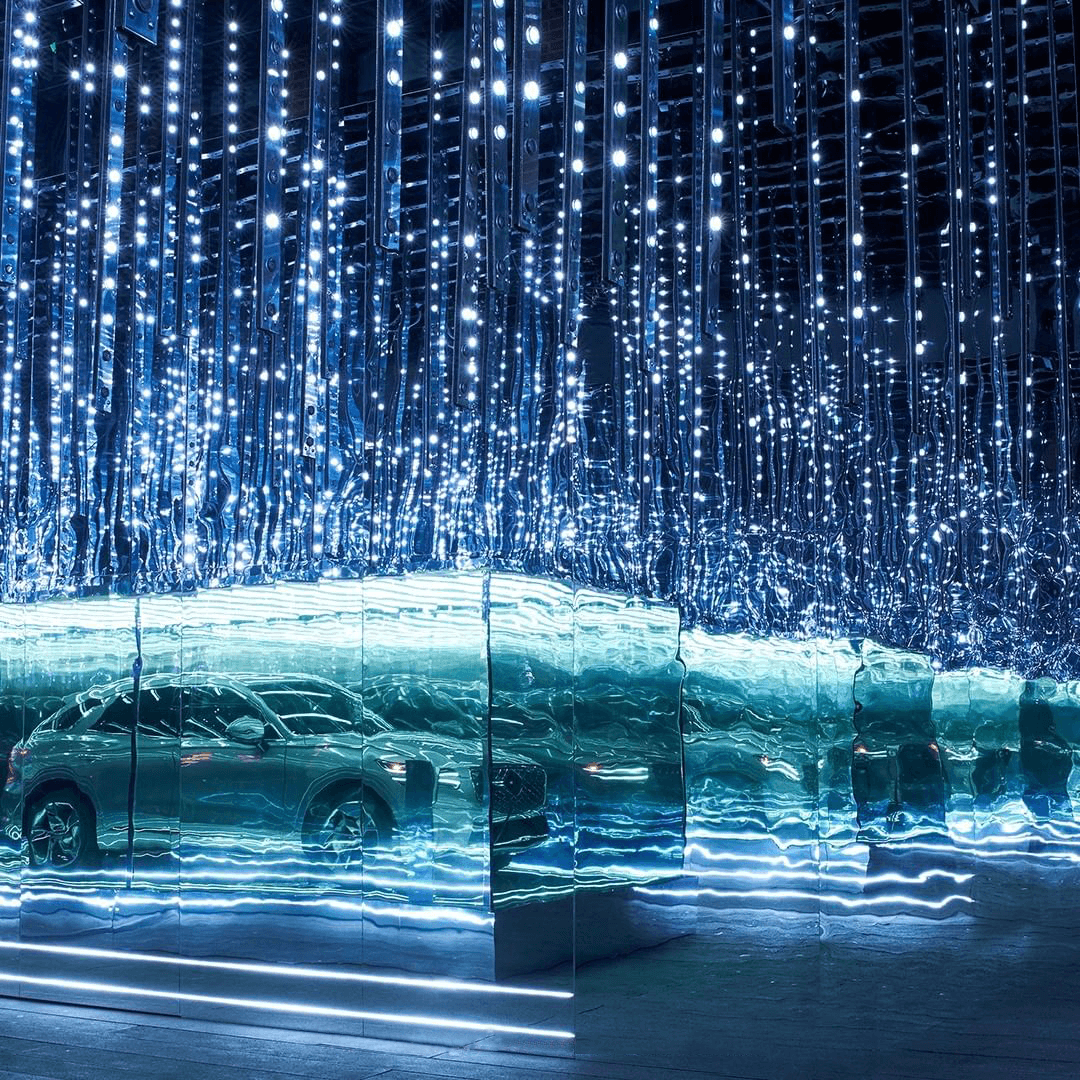 A car reflected in mirrored panels beneath a canopy of blue-white string lights hanging from the ceiling.