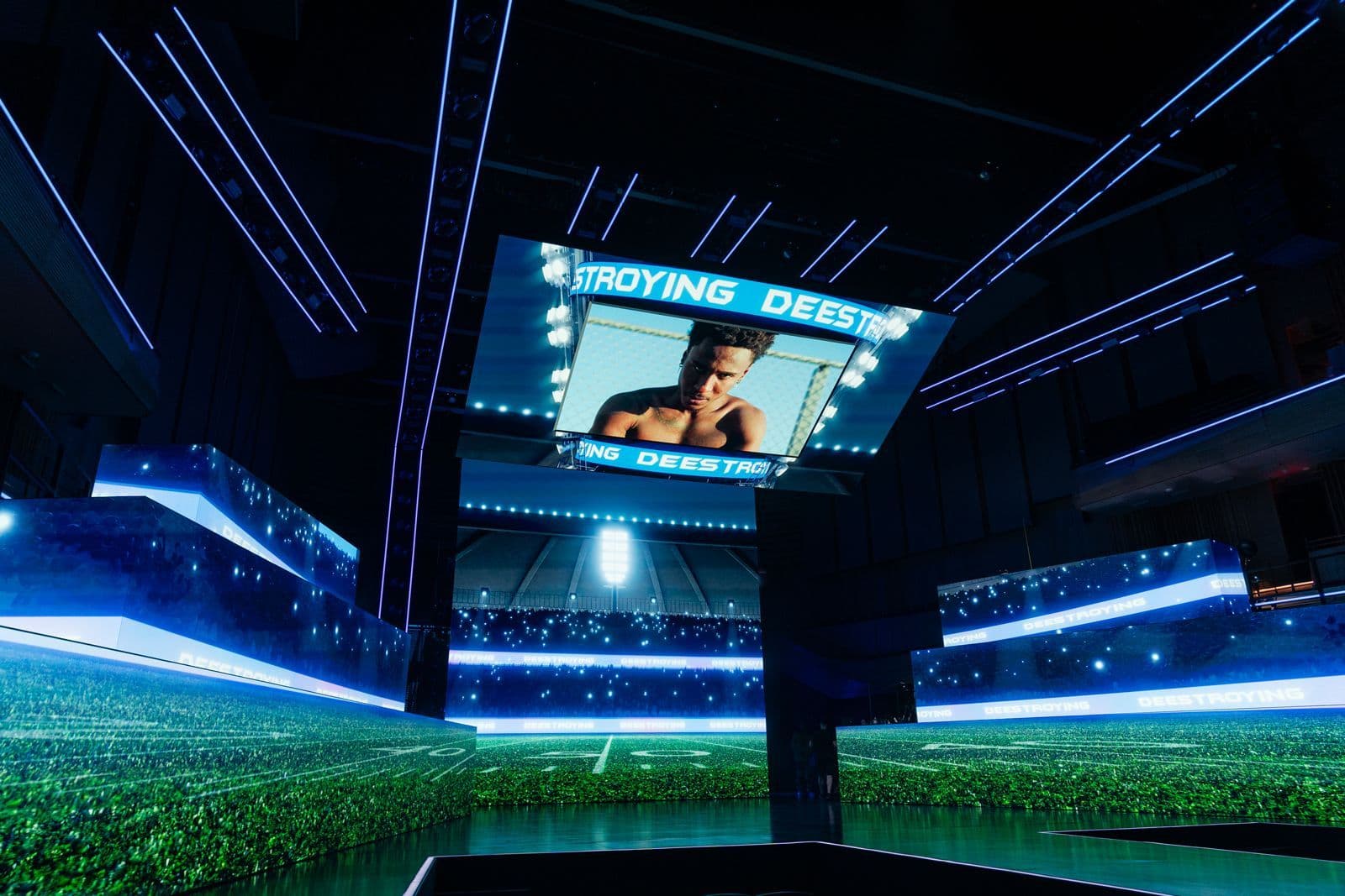 Wide stadium-style stage screens showing a portrait, lit in blue and green