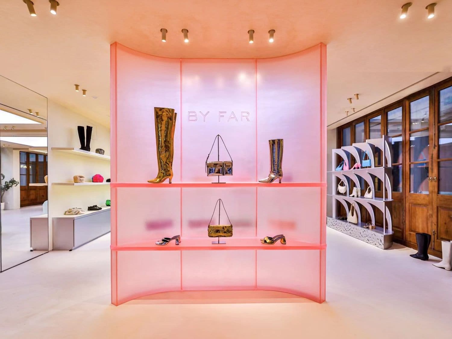 Pink glass display case holding shoes and boots inside a store, with wood shelving in the background