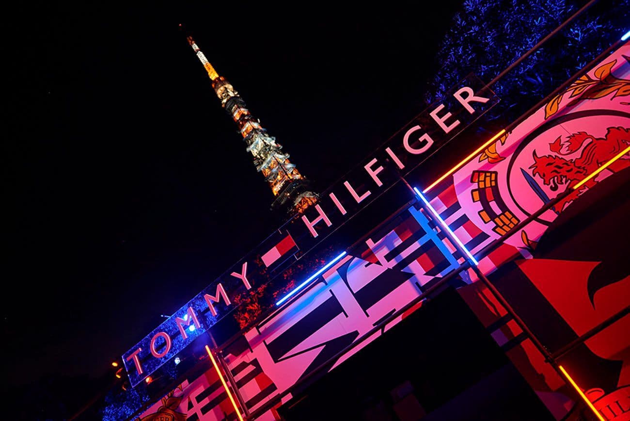 Illuminated Tommy Hilfiger sign beneath Tokyo Tower at night, framed by red and blue neon lights.