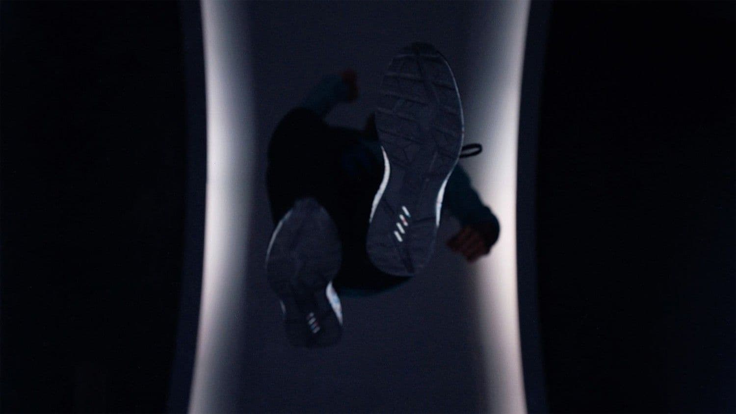 Close-up of the sole of a running shoe silhouetted against a softly lit circular tunnel backdrop.