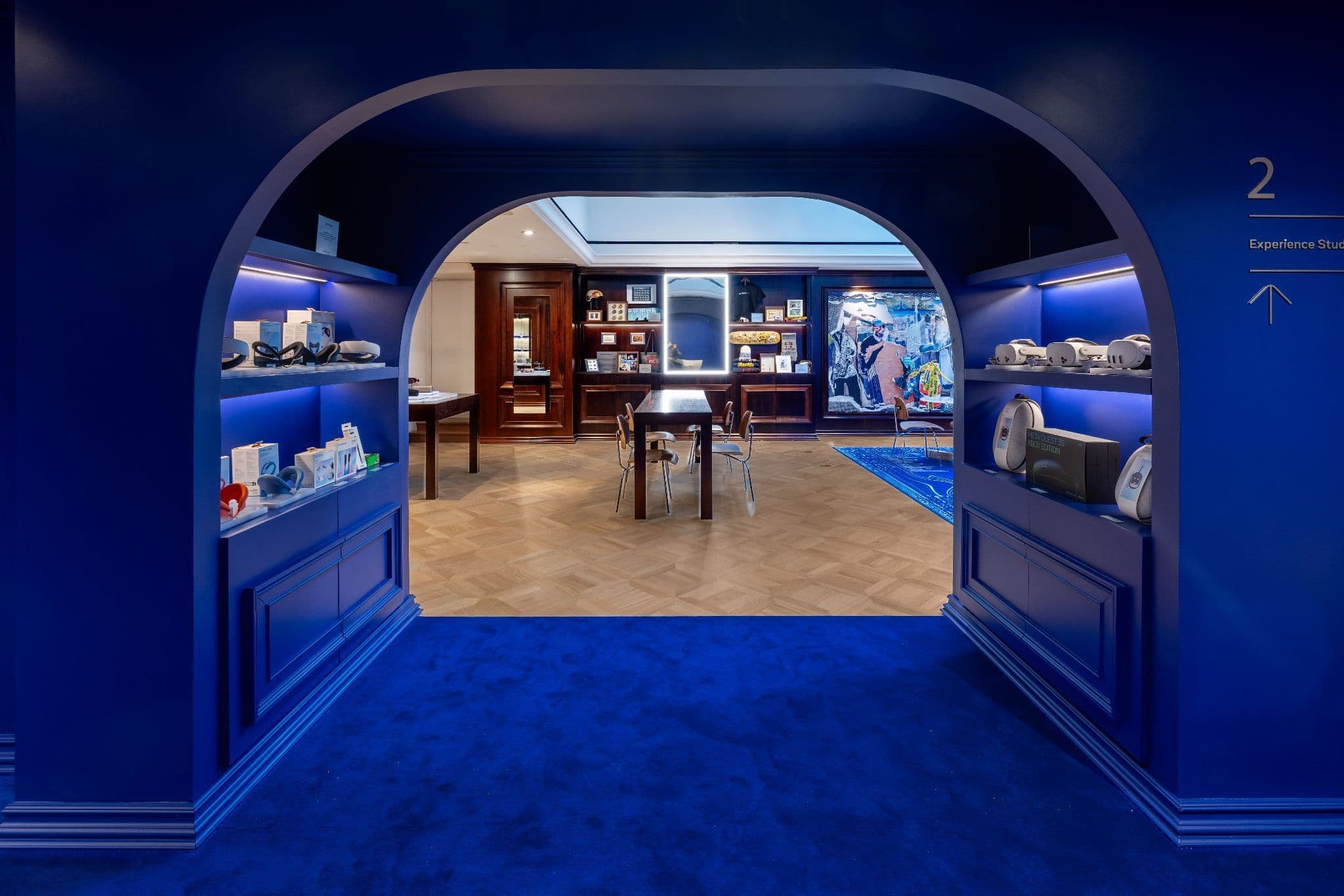 Arched blue doorway leading into a shop room with glass display cases and a central table on herringbone flooring.