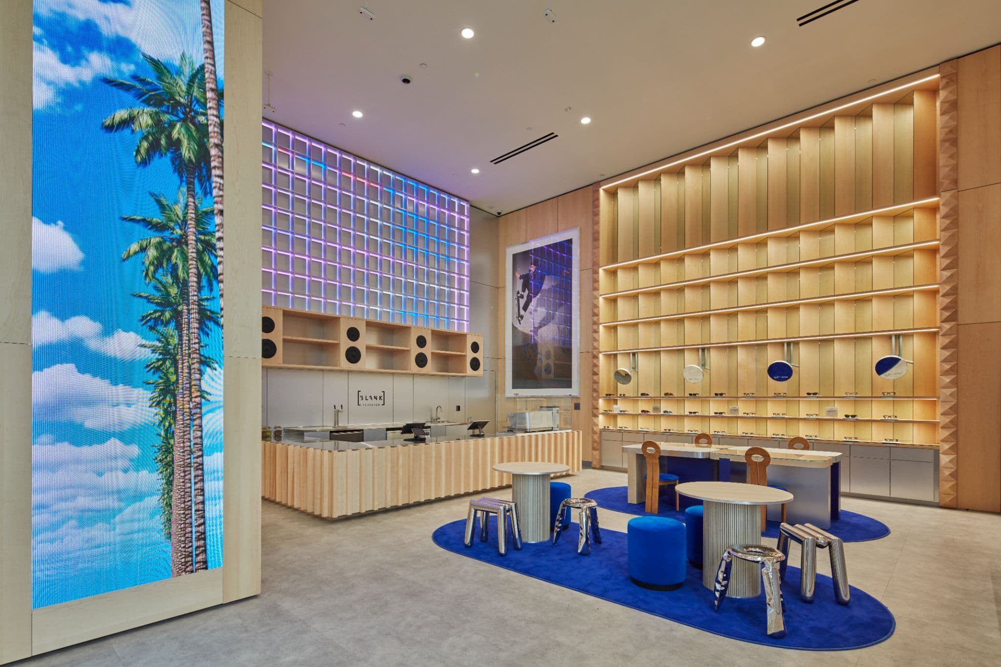 Wood-paneled nook with a backlit palm-tree graphic panel, ribbed shelving, and stools arranged on a blue rug.