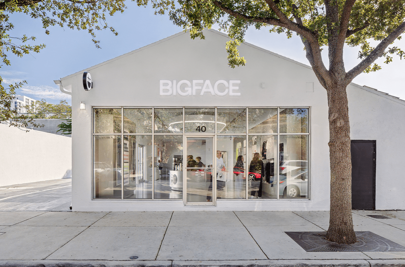 Exterior of the Bigface store with white signage, glass storefront, and a tree out front