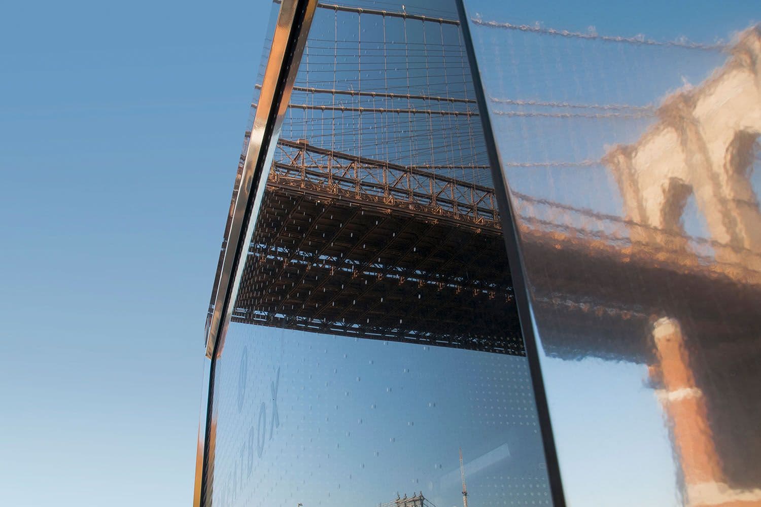 Reflection of the Brooklyn Bridge in the truck's angled glass panel against a blue sky
