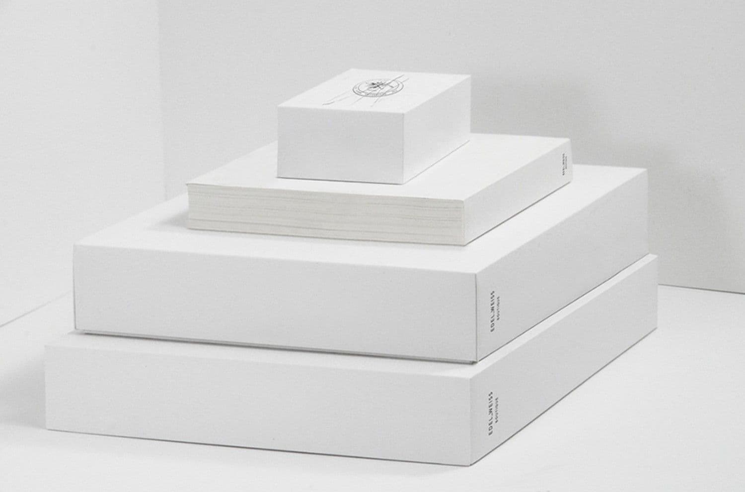 Nested white boxes stacked pyramid-style, topped with a round box stamped with a circular emblem seal, beside a stack of paper.