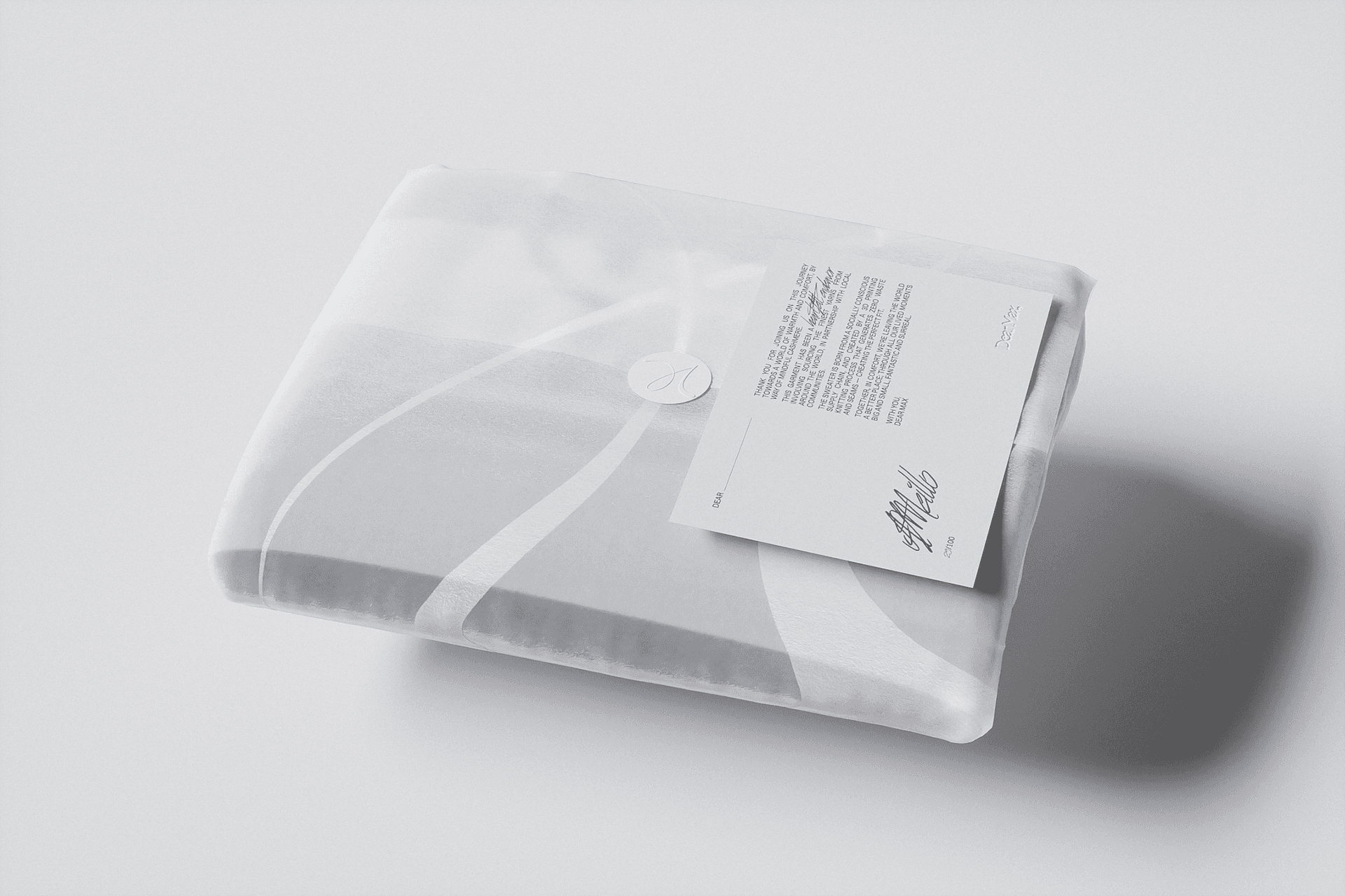 Folded cashmere garment wrapped in translucent packaging with a signed card tucked under the string closure.