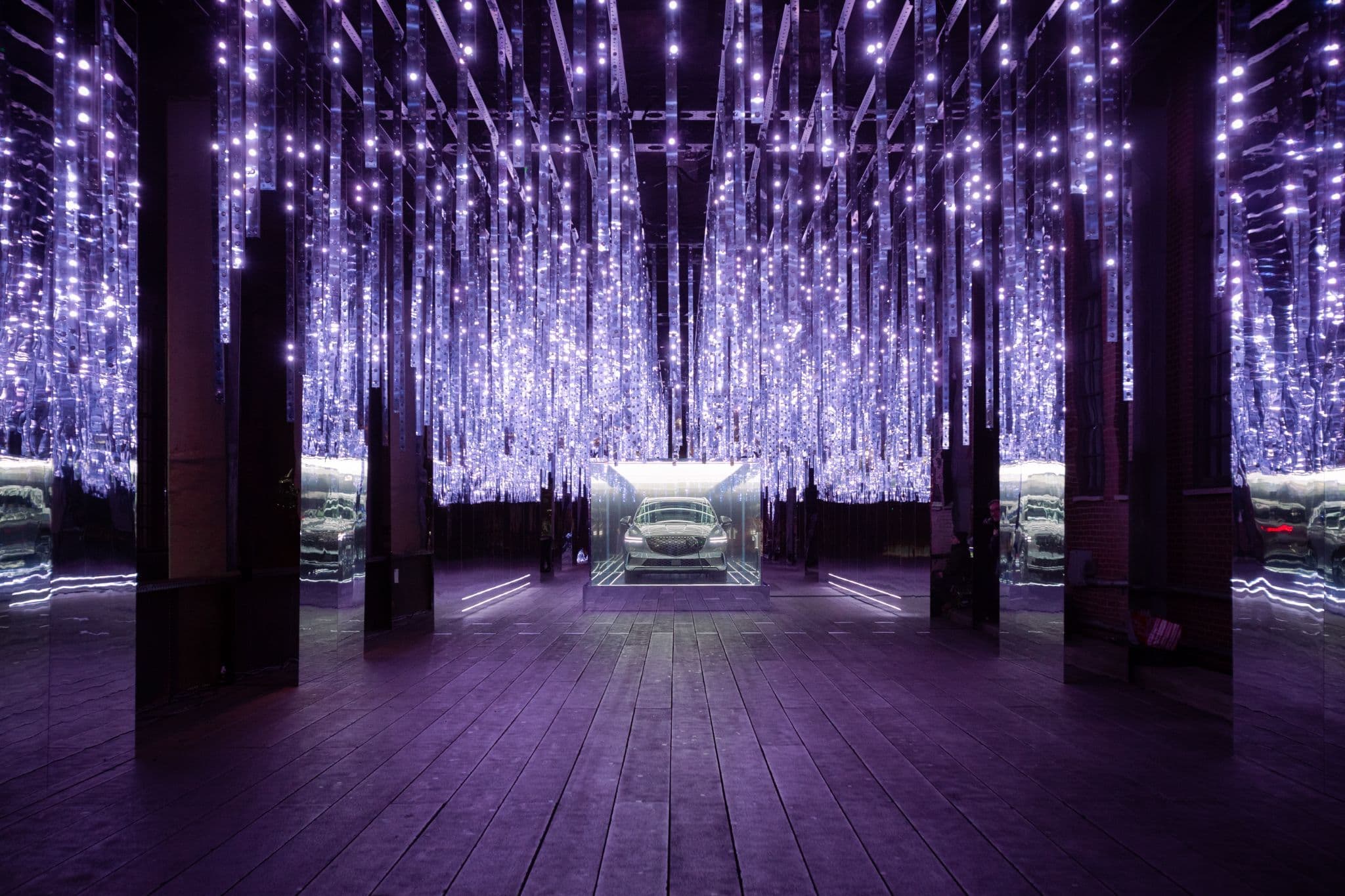 A car centered in a boxy mirrored frame against a backdrop of hanging red string lights, viewed straight on.