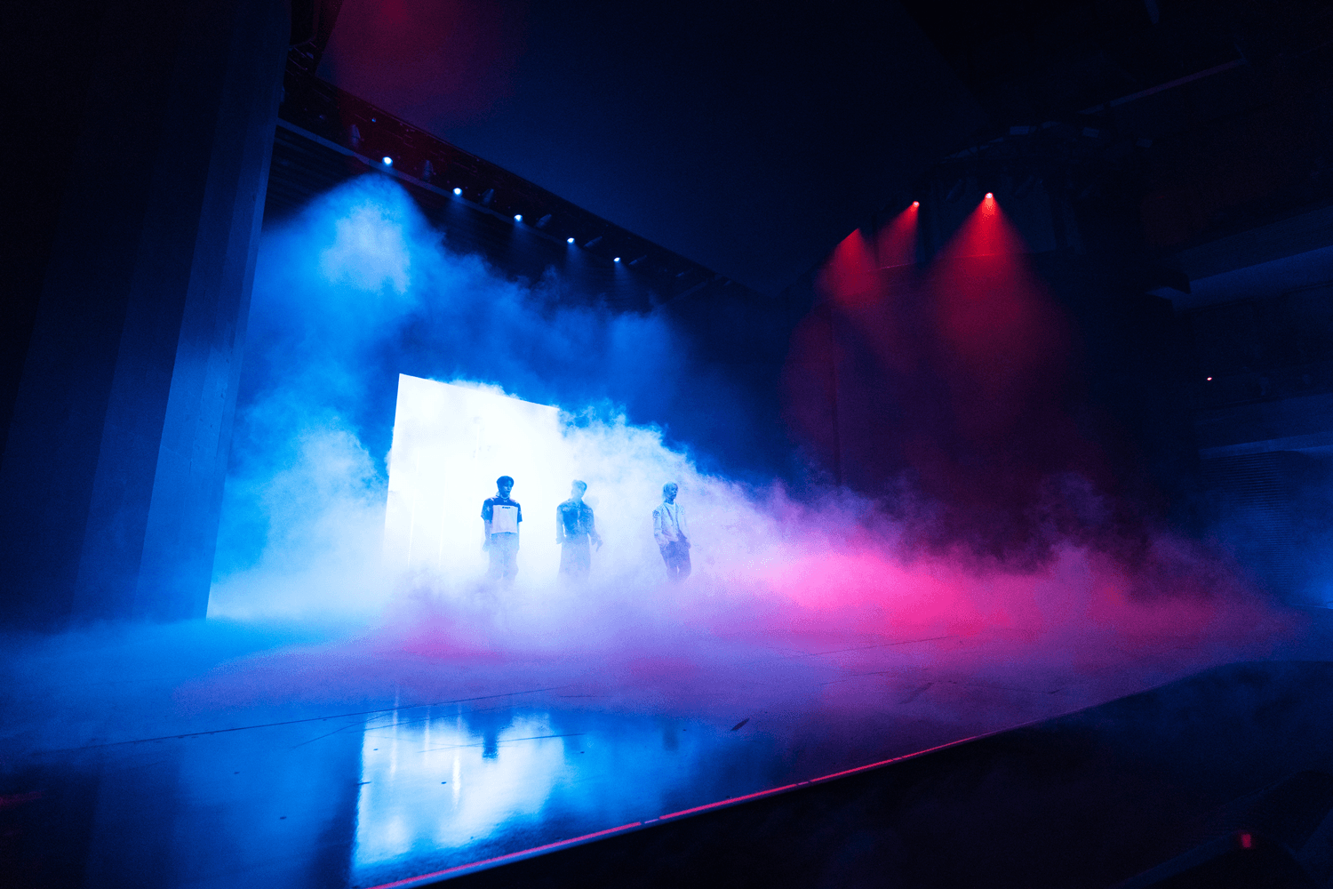 Performers on a misty stage lit in pink and blue with layered screen panels behind