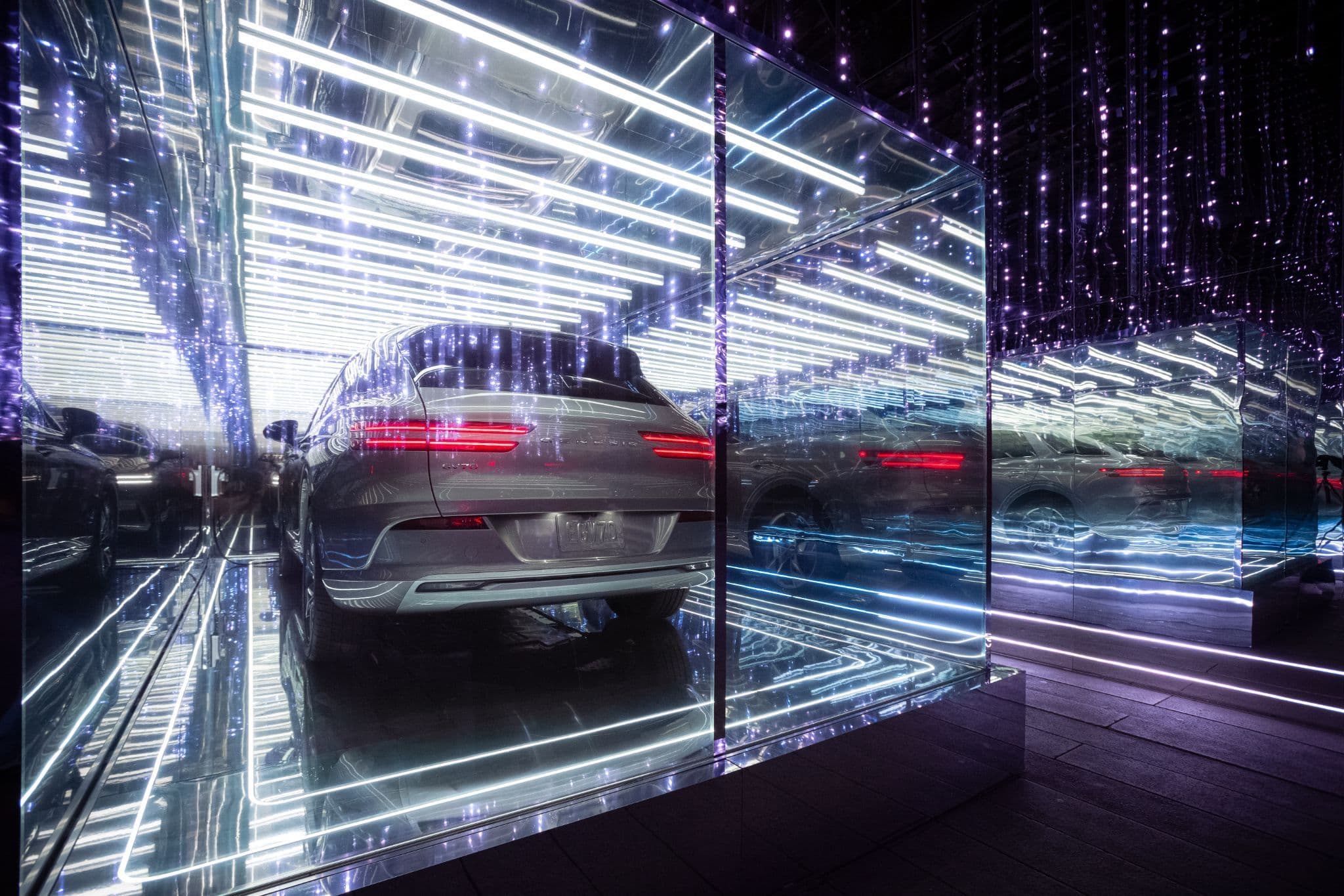 A car repeated diagonally across faceted mirror panels with a hanging red string-light curtain behind it.