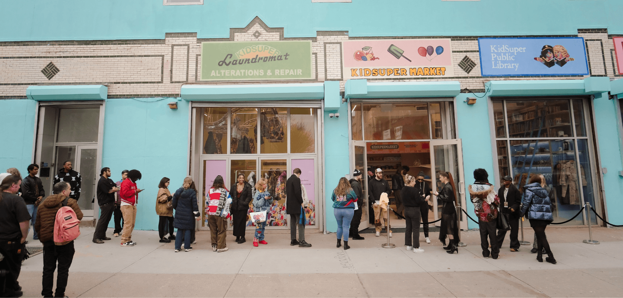 Turquoise storefront facade with signage and a line of people queuing outside on the sidewalk