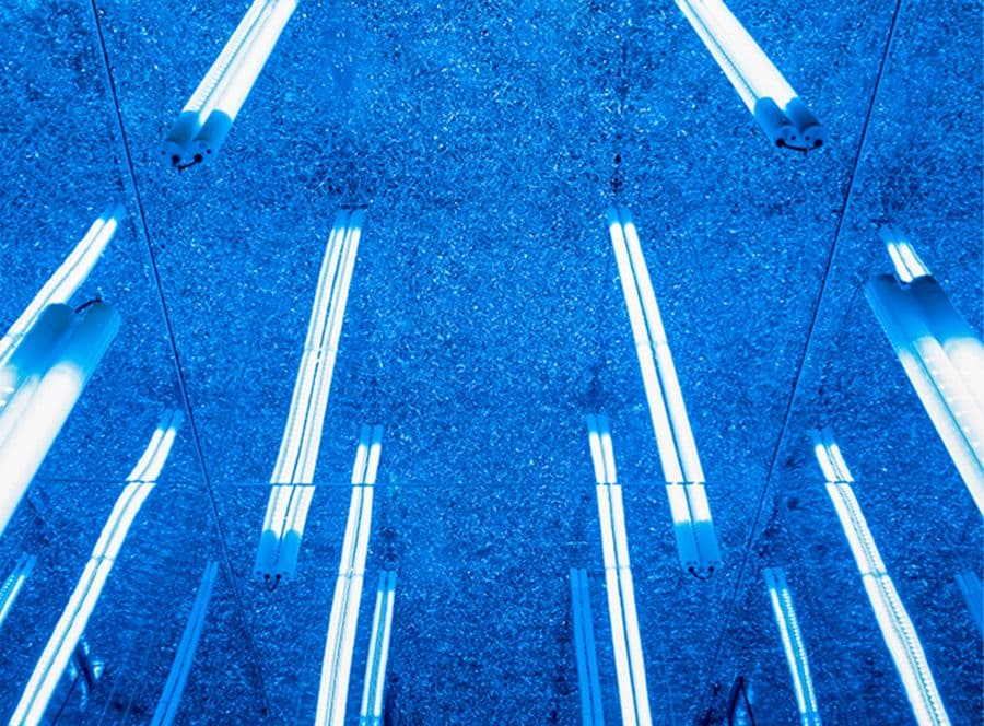 Mirrored ceiling reflecting rows of vertical fluorescent blue light tubes.