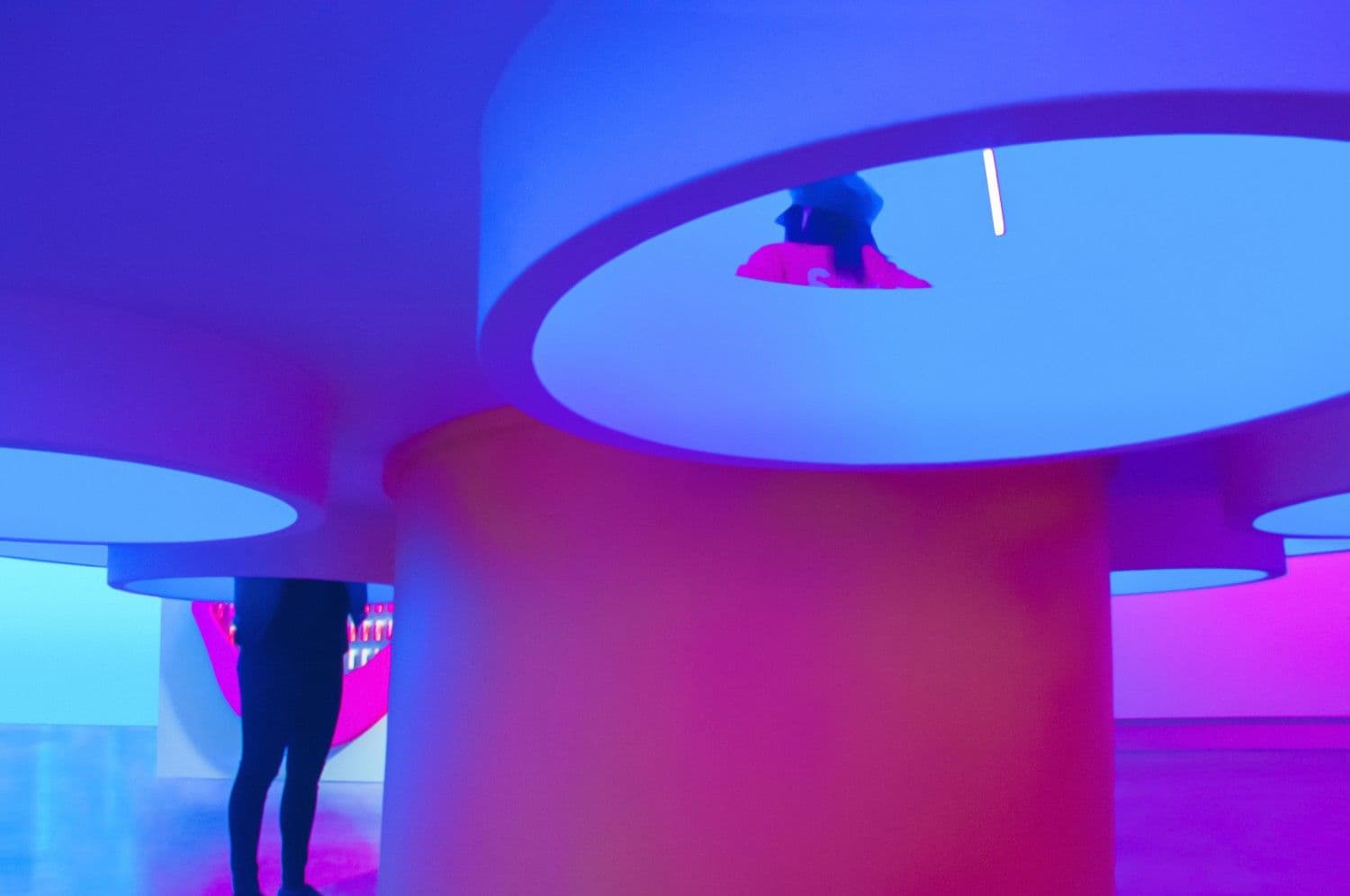 Blue rounded pedestal structure with a person's silhouette standing behind pink lighting.