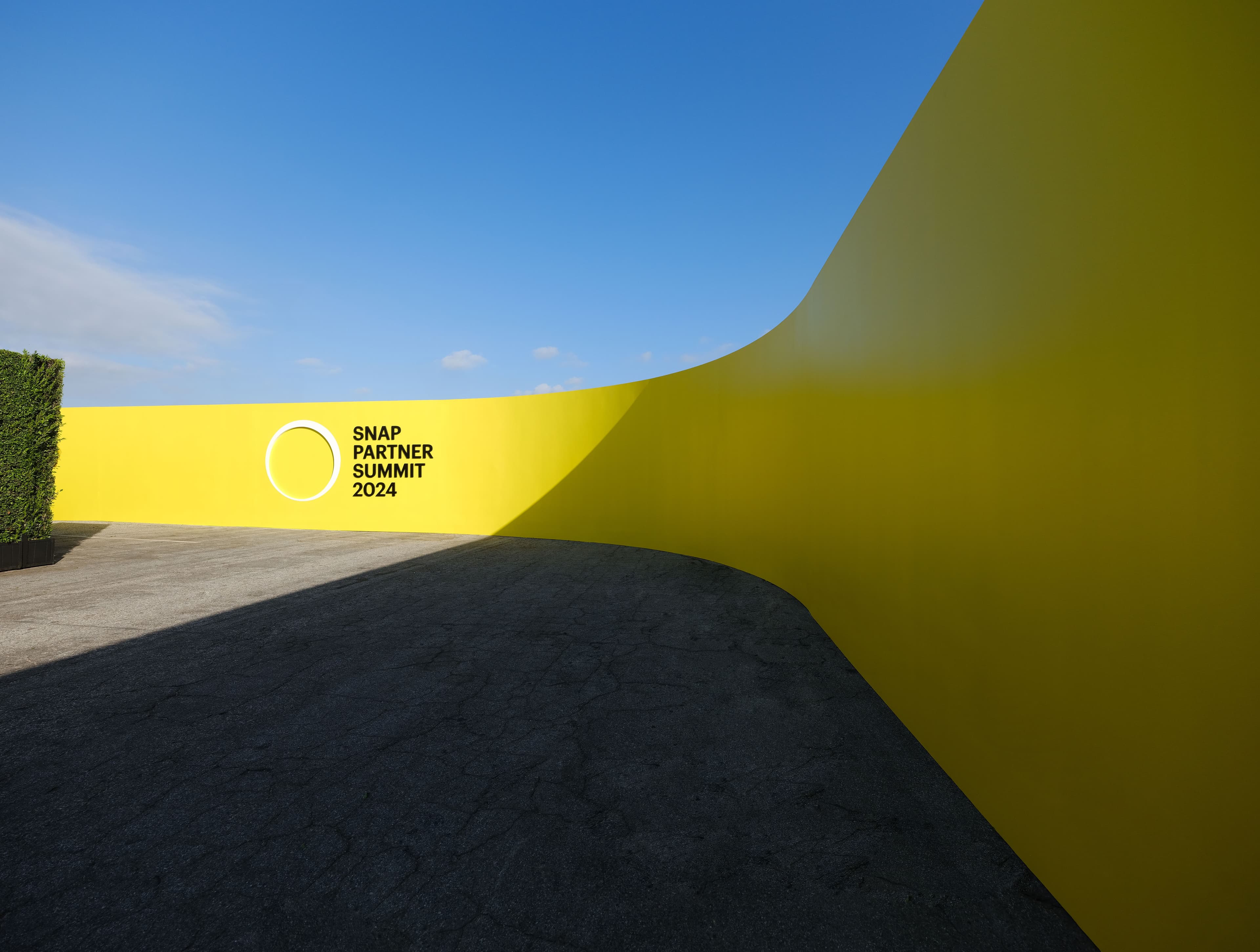 Curved yellow walkway or ramp cutting across a paved outdoor area under a blue sky.