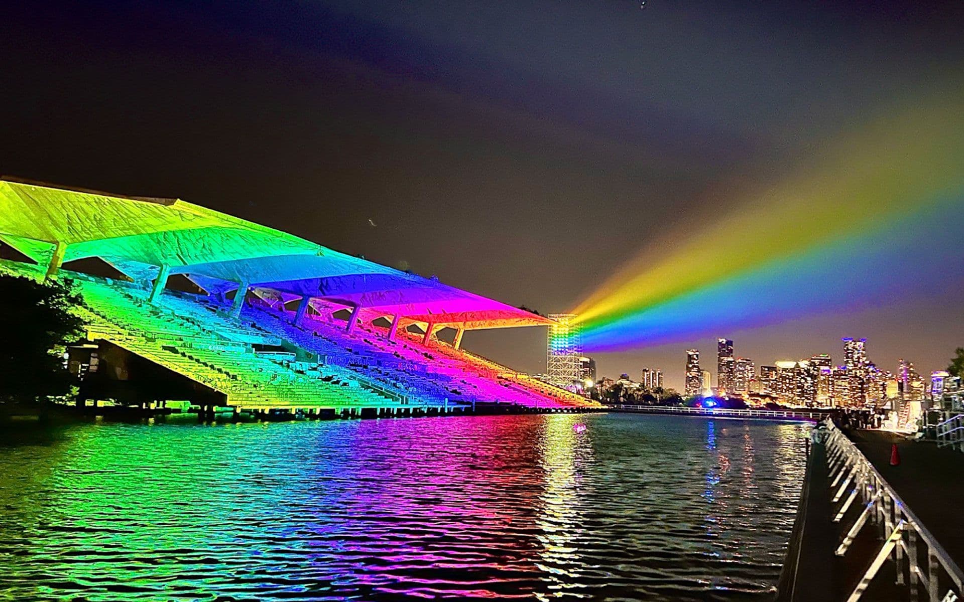 Green neon light beams crossing angular support structures with palm trees silhouetted below