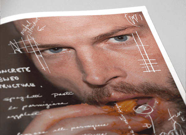 Close-up book page of a bearded man's face eating food, surrounded by handwritten notes and sketched grid marks.
