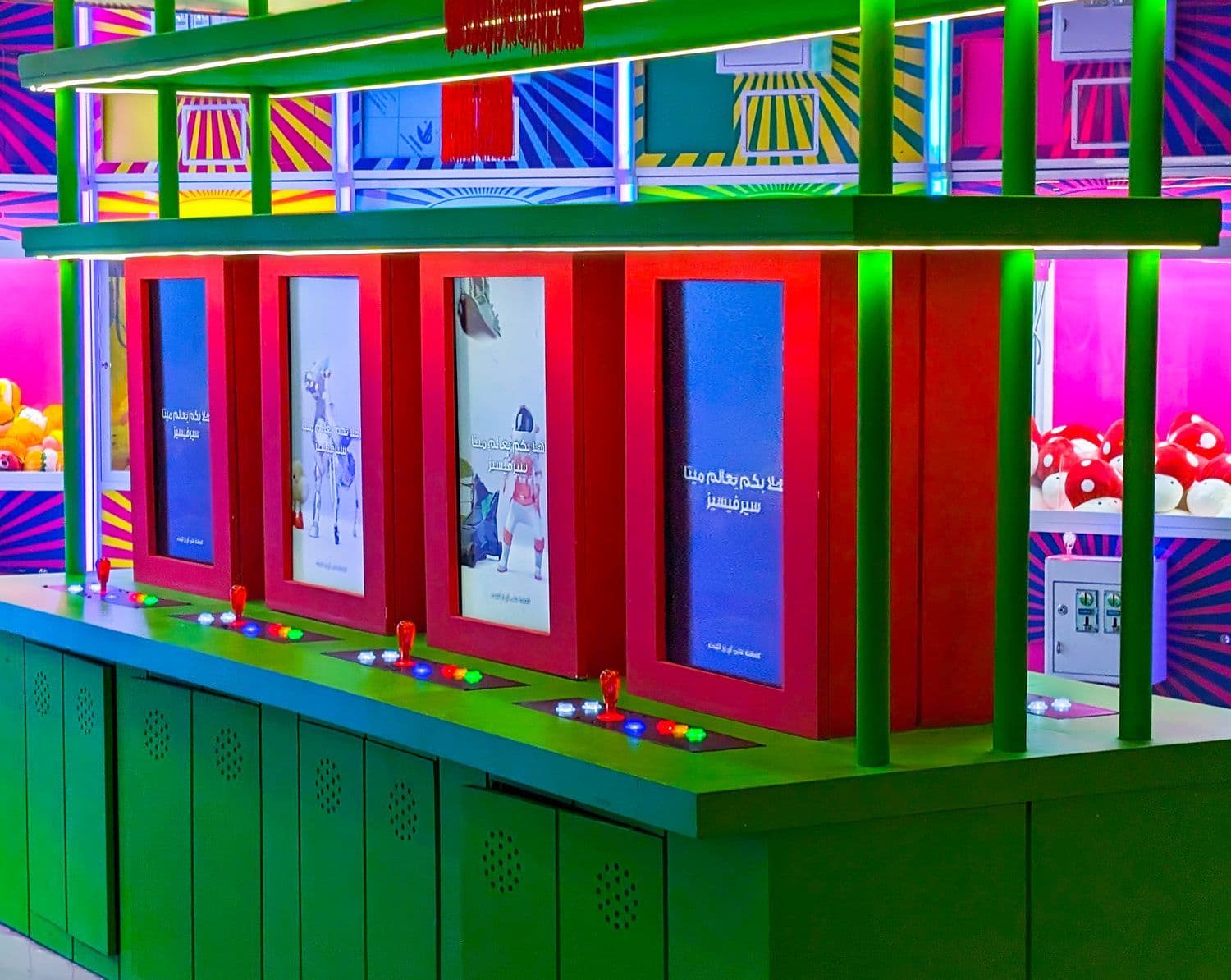 A colorful arcade interior with green shelving, red-framed video screens, and arcade game cabinets along the floor.