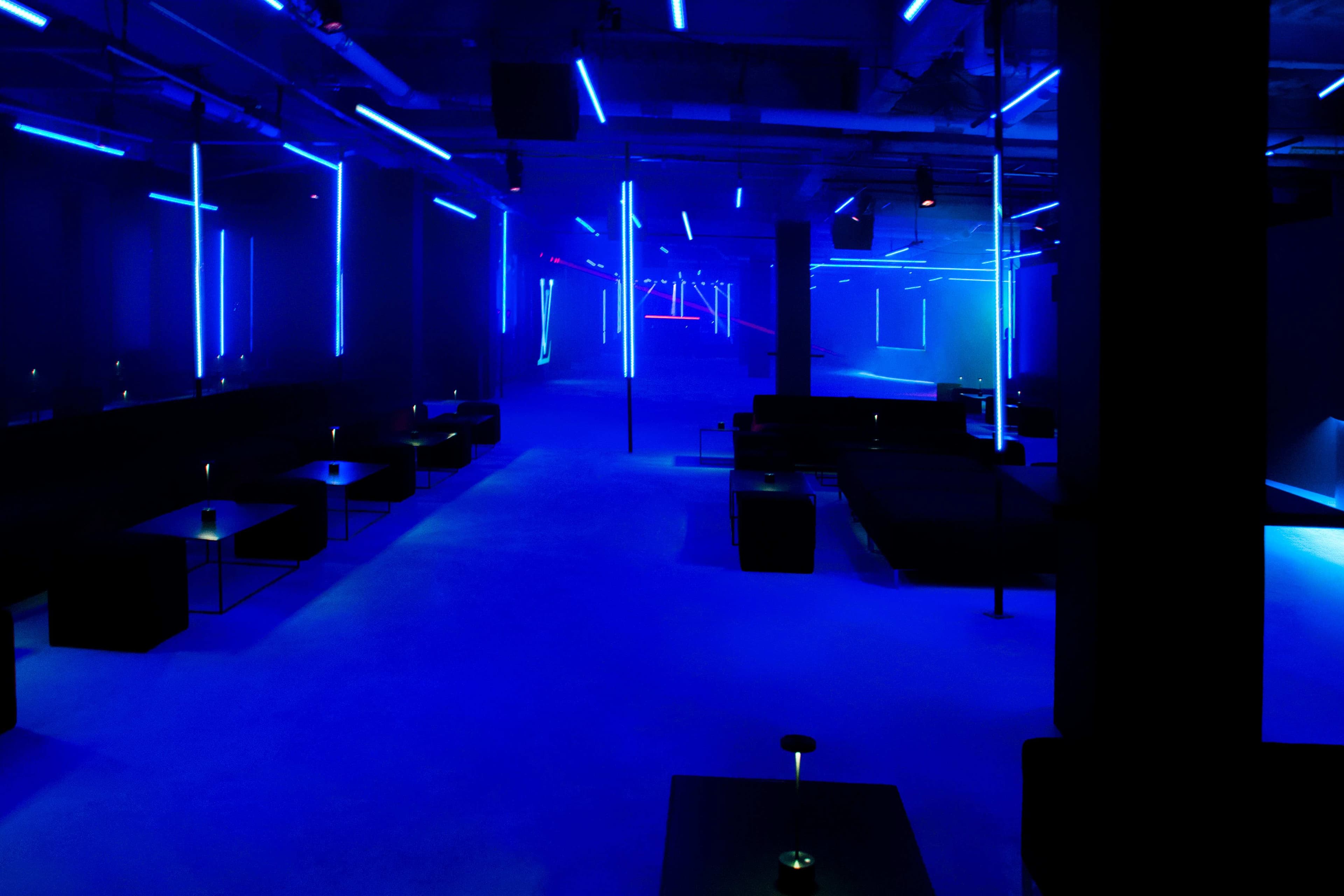 Dark lounge area with blue neon ceiling strips, low seating, and a central pillar.