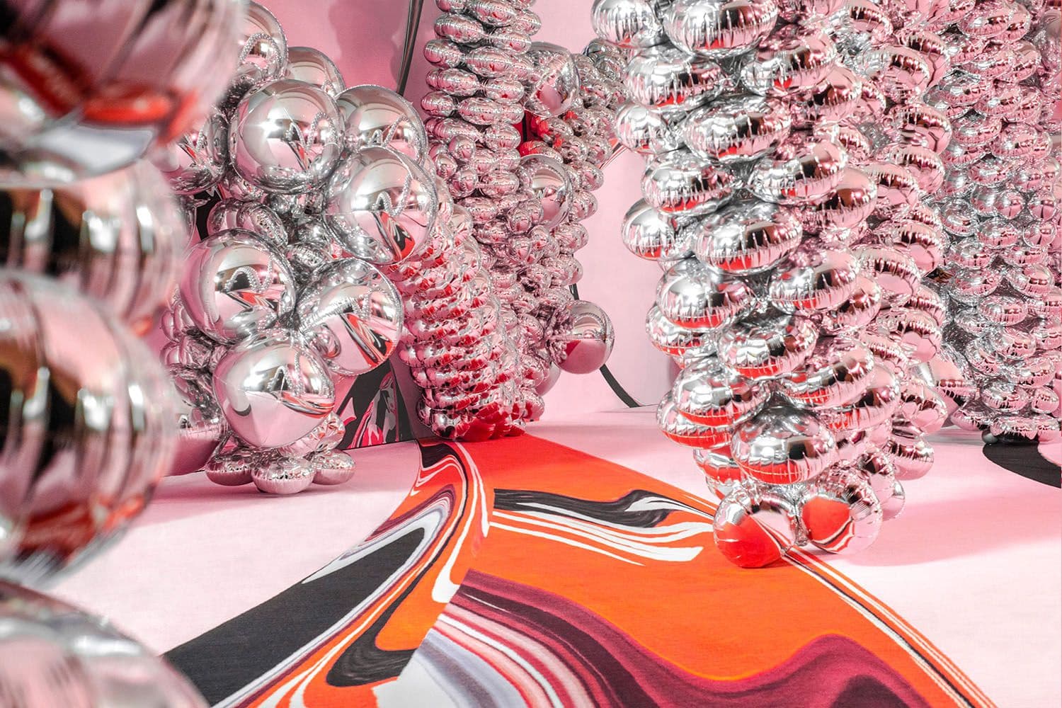 Clusters of silver spiral bead sculptures on a pink surface beside a swirled orange, black and white abstract print