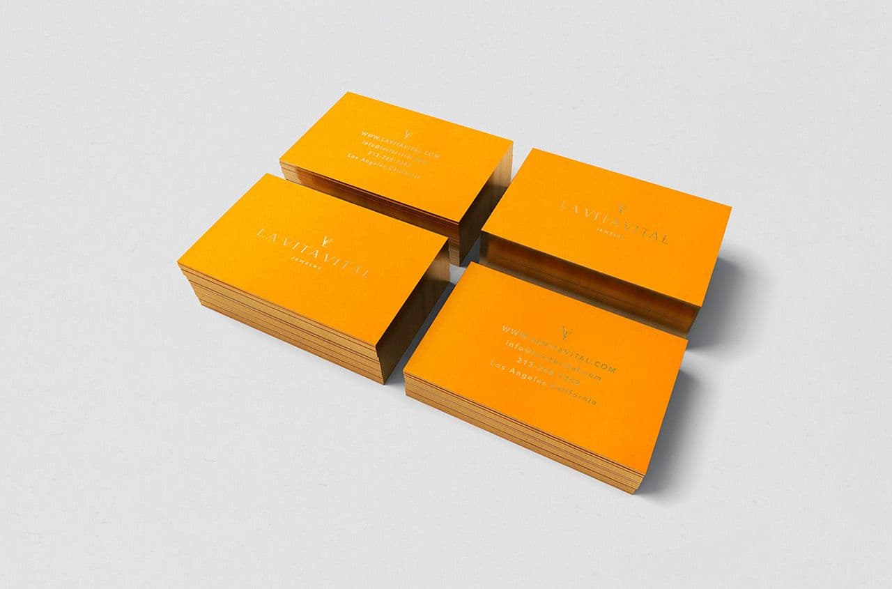 Four orange business cards with gold foil text and logo, stacked in two facing pairs on a light gray surface.